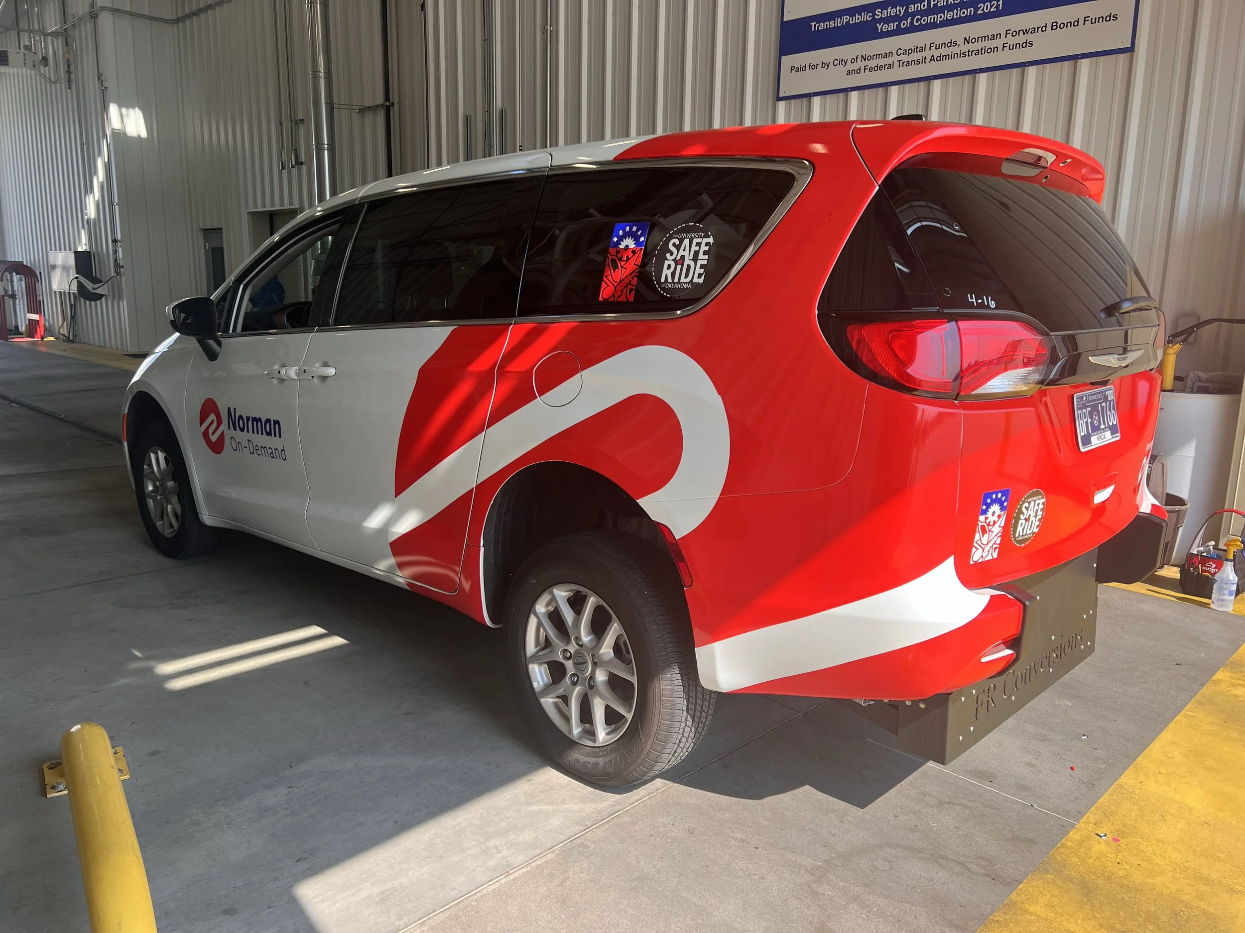 A red and white Norman On-Demand vehicle parked indoors, with safety stickers on the window and a yellow parking block nearby.