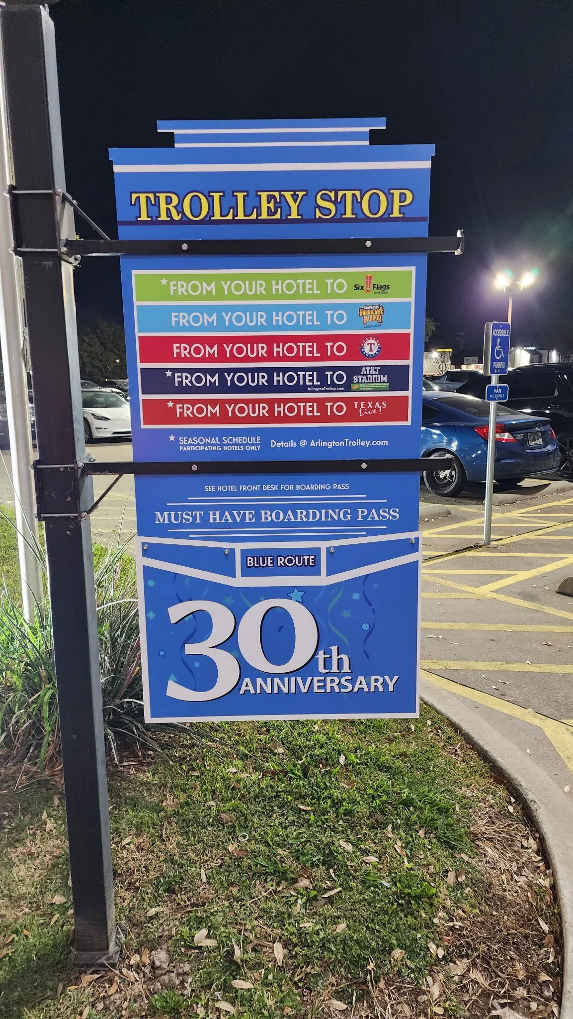 Sign celebrating the 30th anniversary with various schedule routes for trolley stops in Arlington, Texas, including routes to Six Flags, Hurricane Harbor, AT&T Stadium, and a red route, with instructions to see the hotel front desk for boarding passes and to have a valid boarding pass.