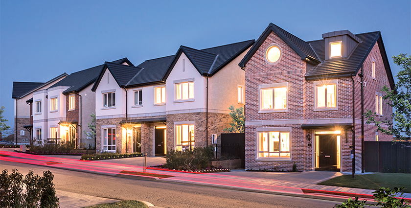Row of modern houses with brightly lit windows and brick exteriors at dusk.
