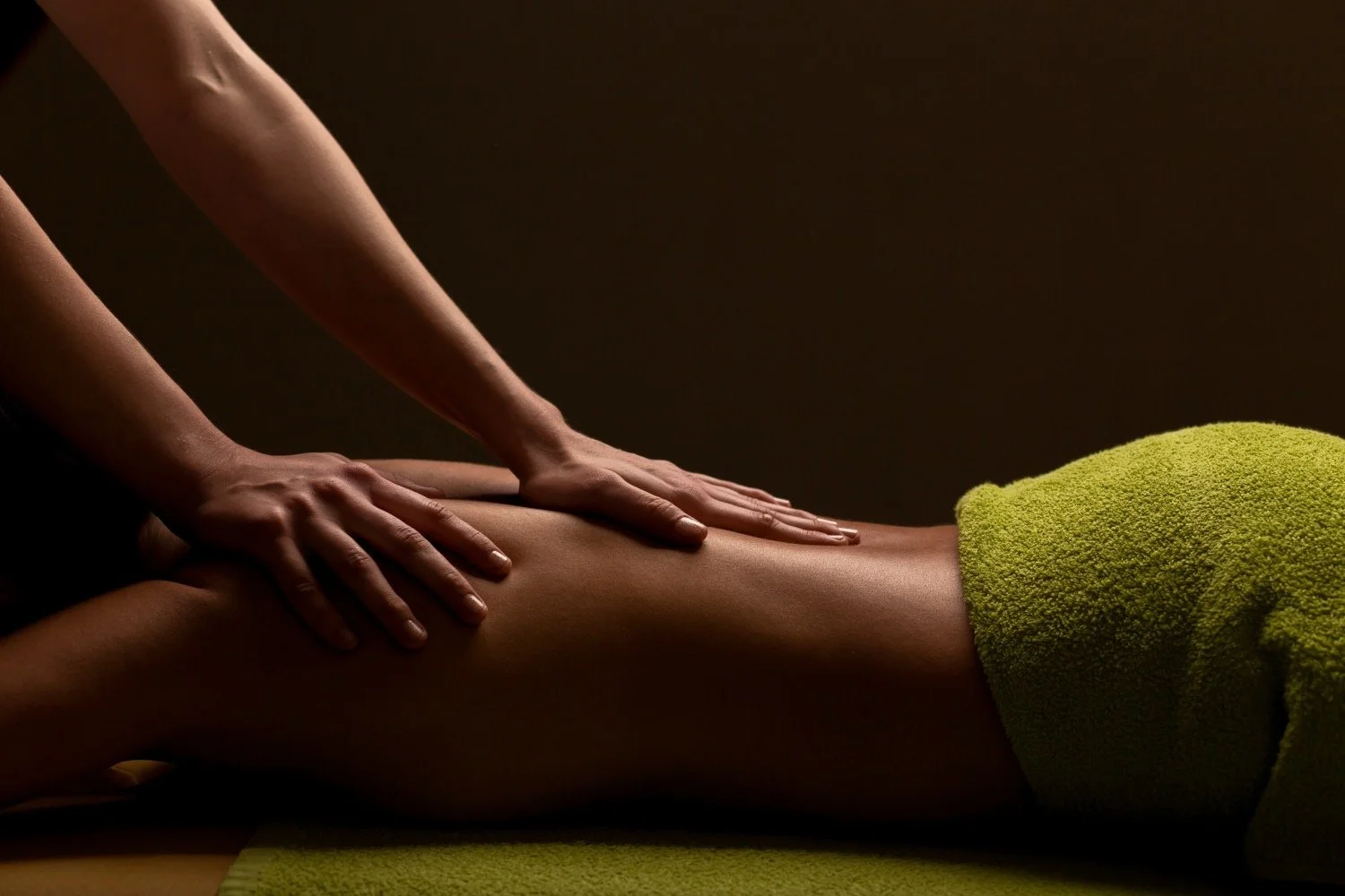 A person receiving a back massage from a massage therapist, with their back exposed and covered by a yellow towel.