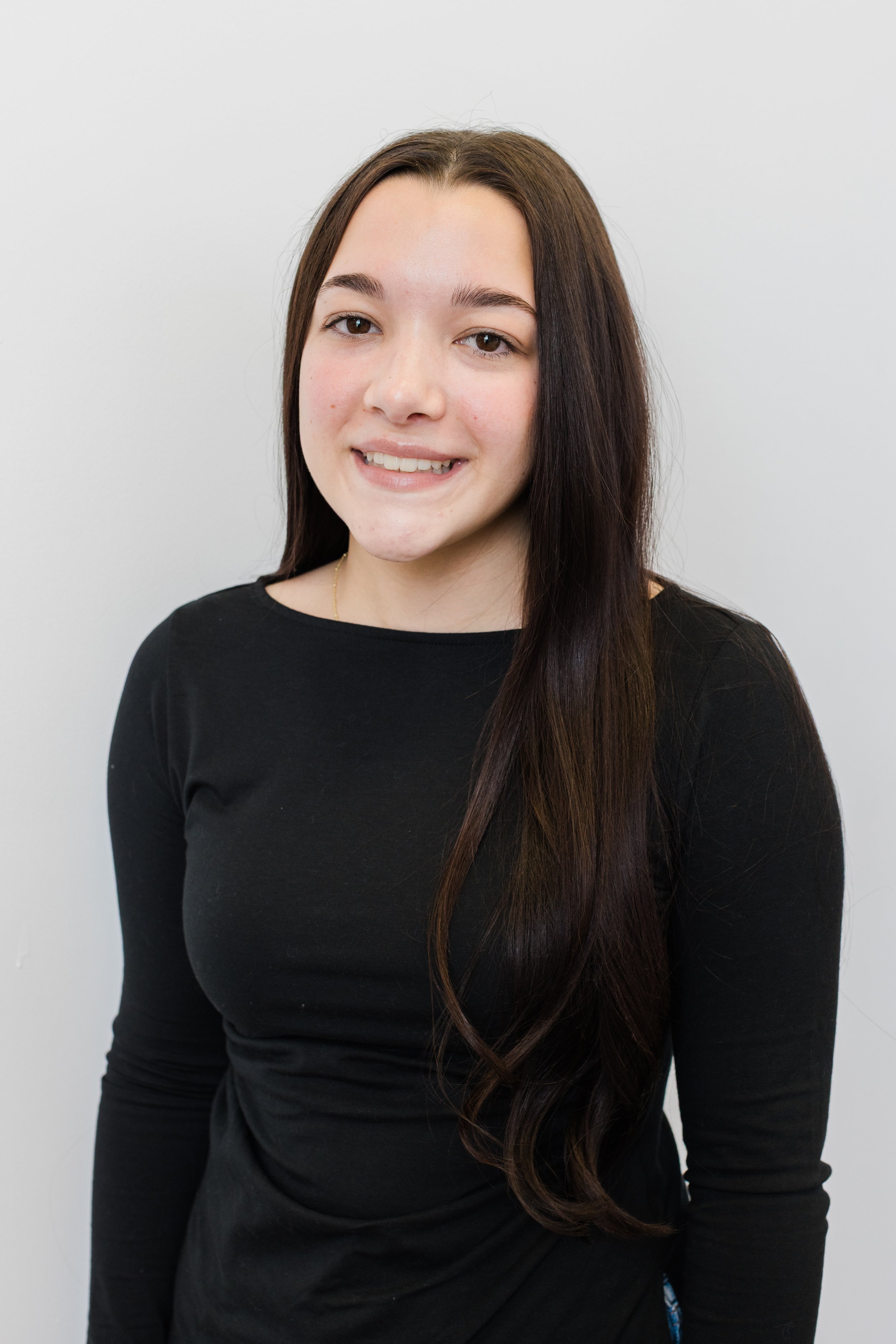 Young woman with long brown hair smiling and wearing a black top against a plain white background.
