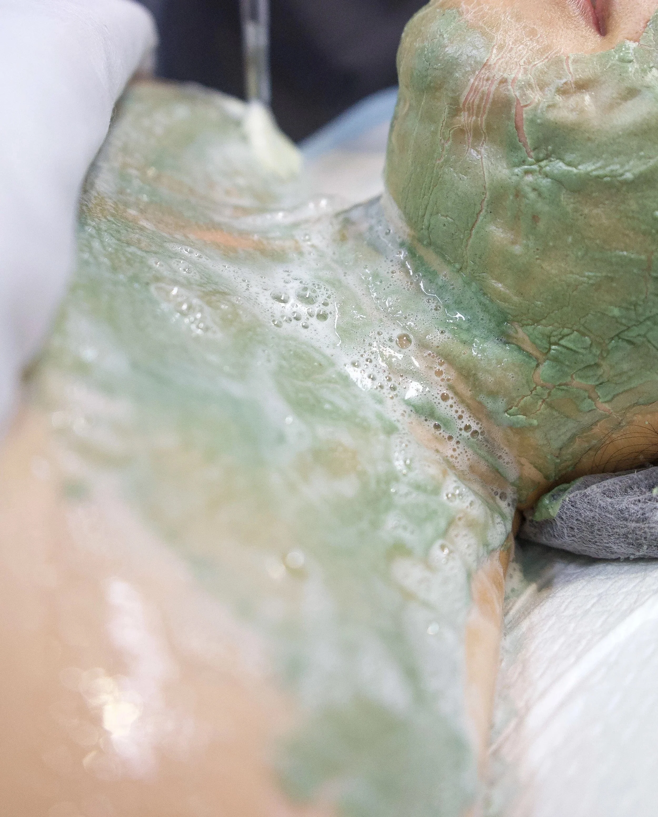 A close-up of someone applying a green and yellow facial mask, with soap foam visible on the face.