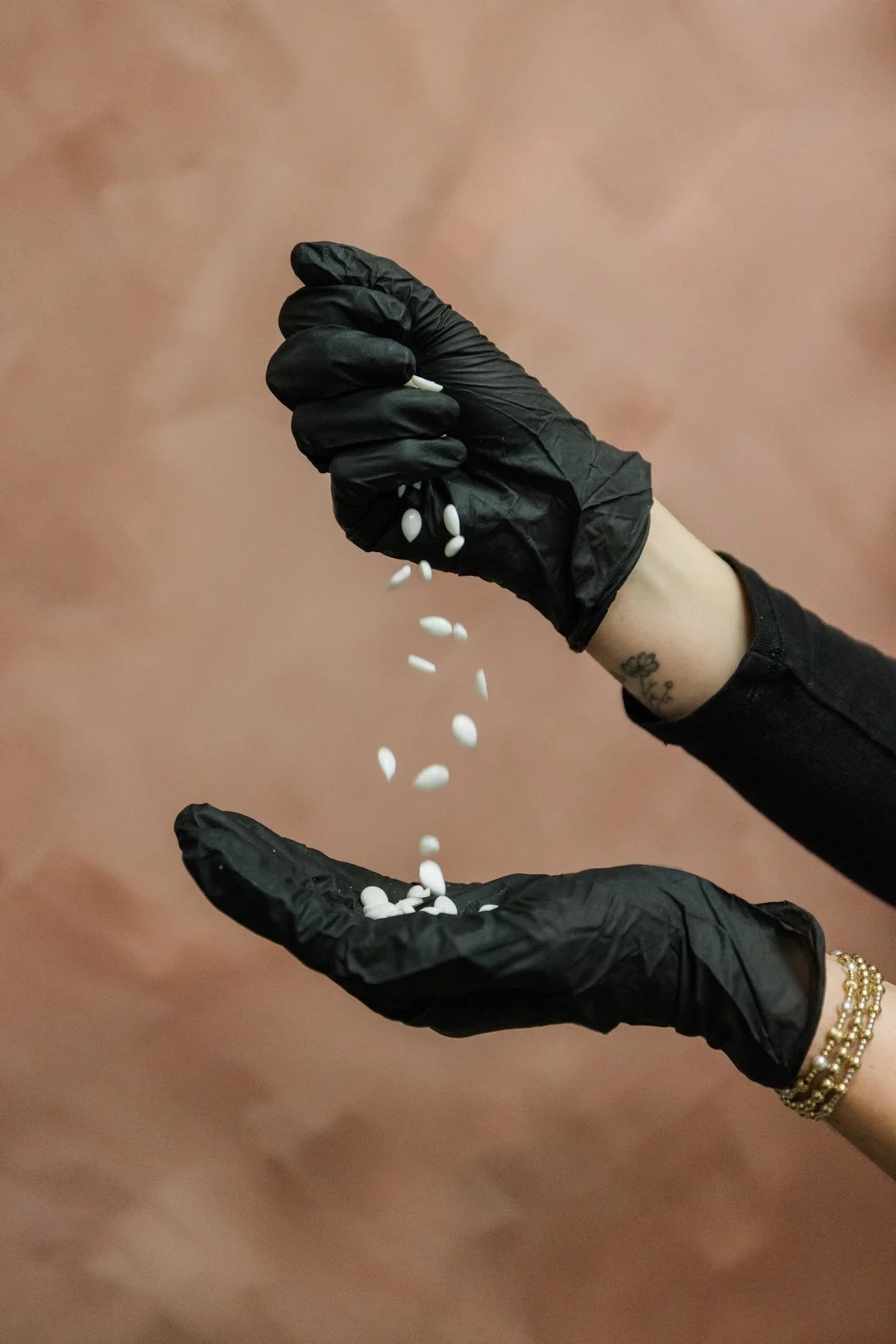 Person wearing black gloves pouring white pills from one hand into the other.