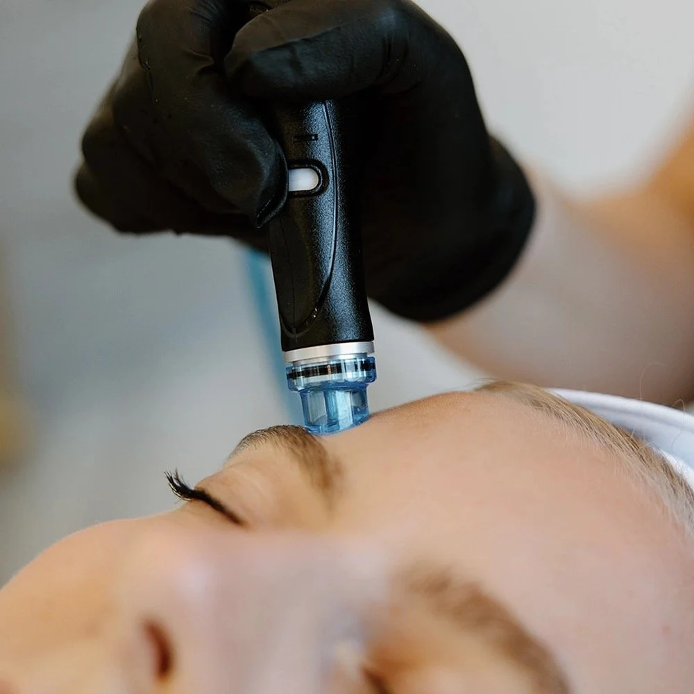A person receiving a facial or cosmetic treatment with a handheld device, while lying down with eyes closed.