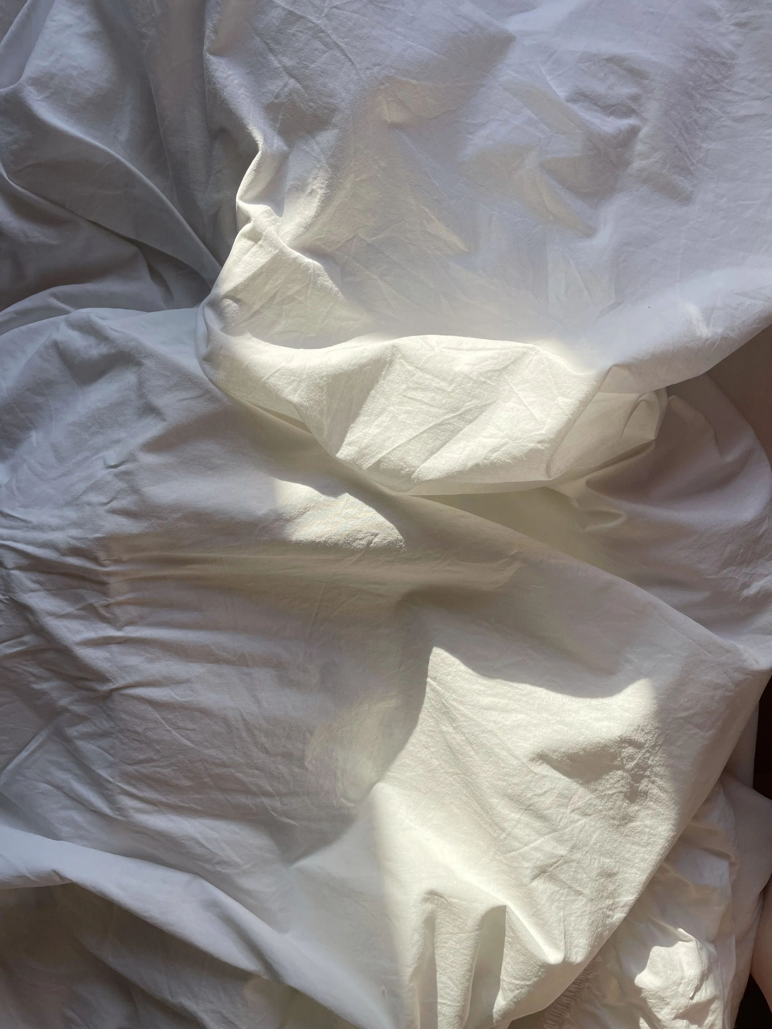 White crumpled bedsheets with some sunlight and shadows.