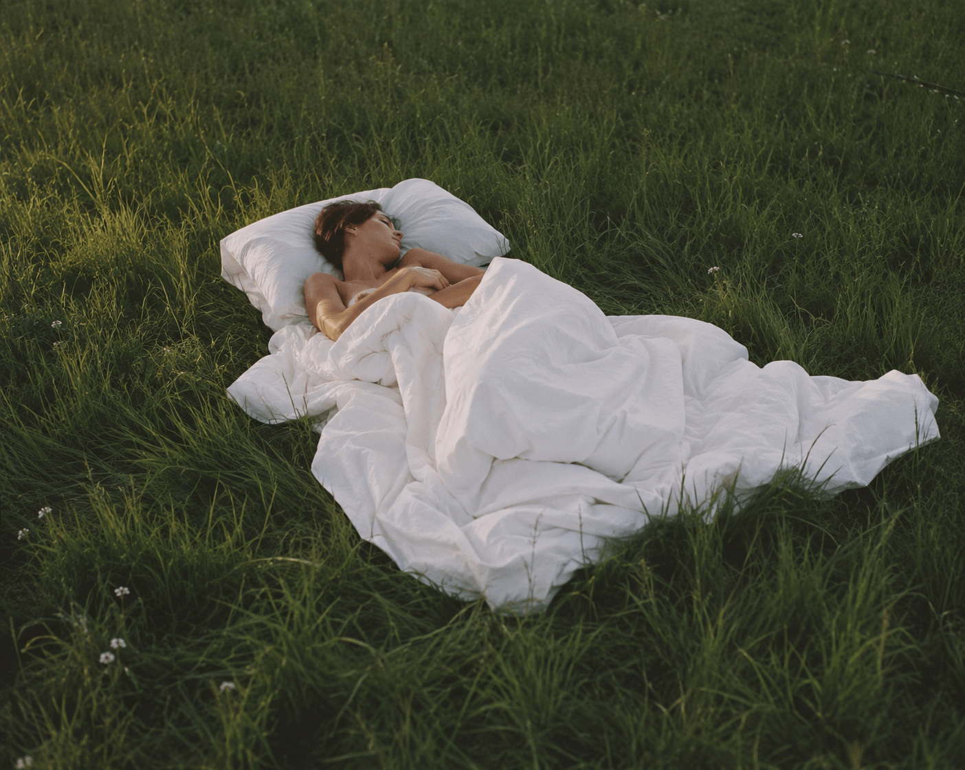Woman lying in the grass with a cushion and a duvet.