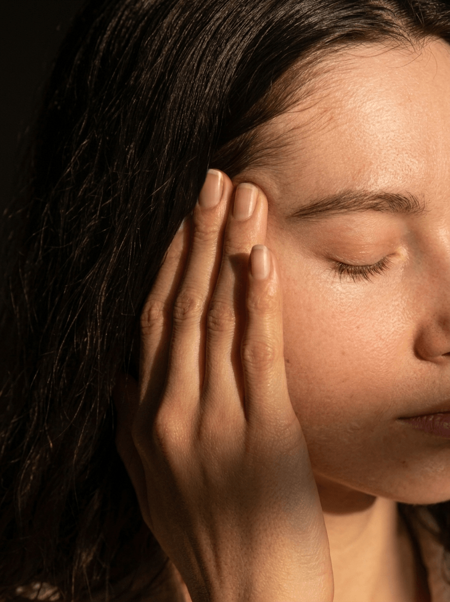 A woman with her eyes closed is holding her temple with her fingers.