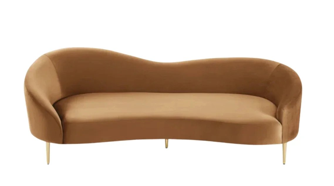 A tan, mid-century modern style sofa with curved armrests and four tapered gold legs.