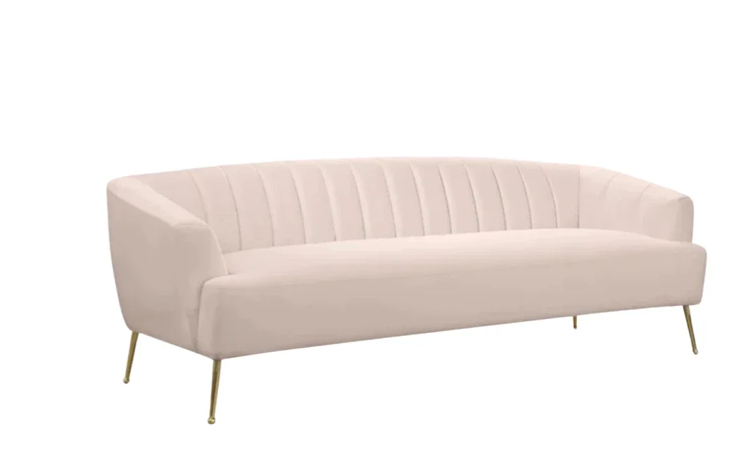 A light pink modern sofa with gold legs against a white background.