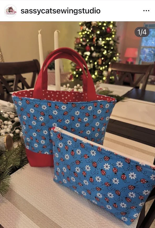 Blue tote bag and matching zippered pouch with ladybug and daisy floral patterns on a table with Christmas decorations, in front of a decorated Christmas tree.