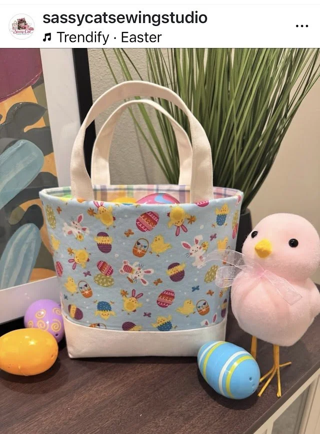 Easter-themed fabric tote bag with a spring bunny and egg pattern, positioned on a table along with pastel-colored plastic eggs and a plush pink chick toy.