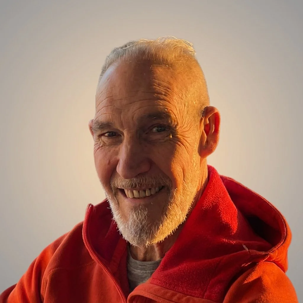 Elderly man with a beard and gray hair, smiling, wearing a red sweatshirt