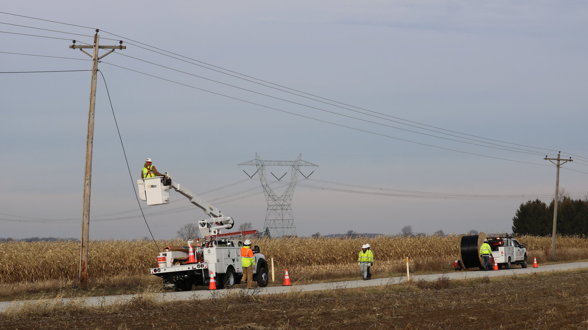 Utility line crew with bucket trucks installing fiber infrastructure along a rural road