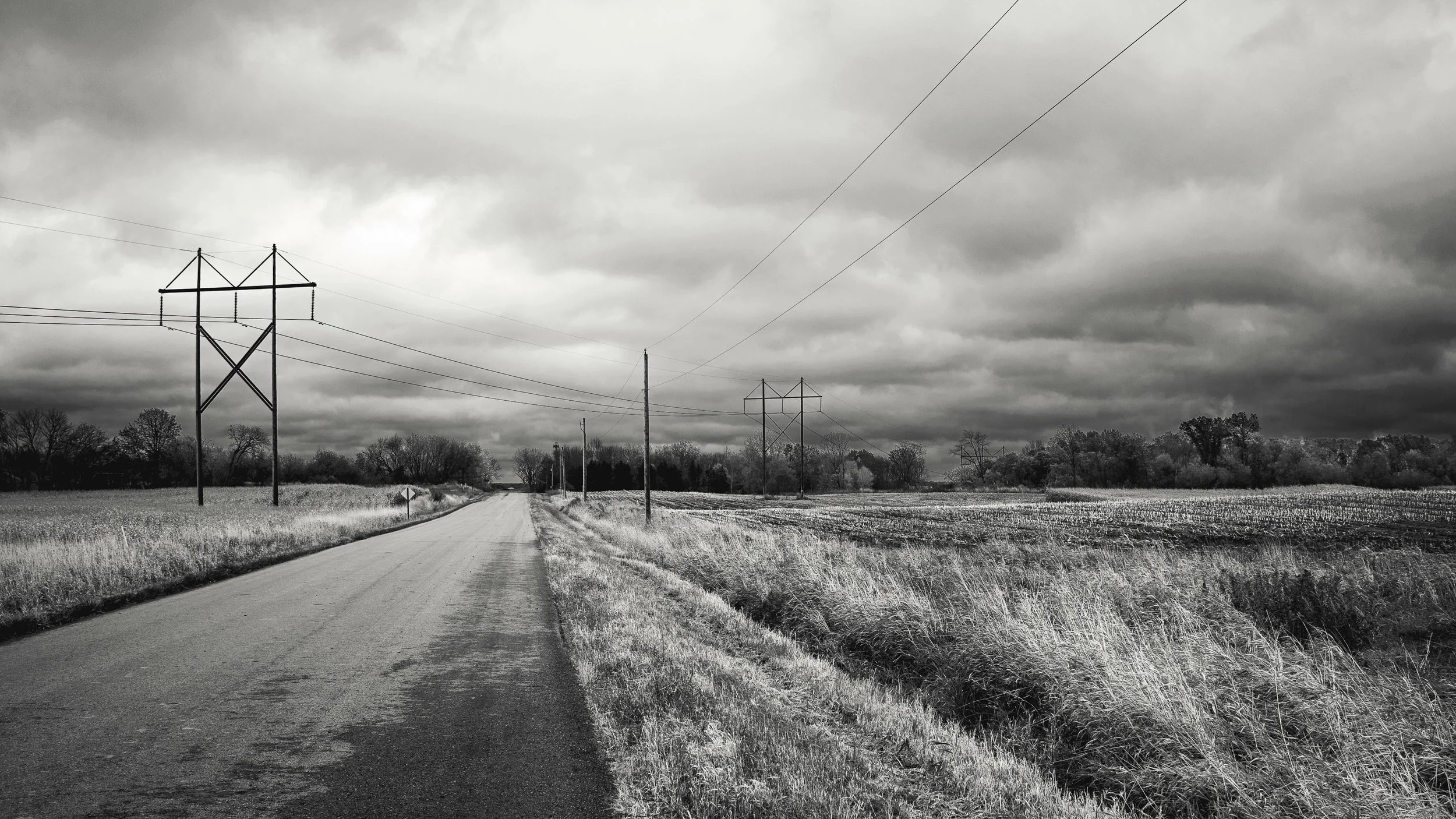 Rural Indiana road with power lines and utility poles stretching into the distance under a dramatic cloudy sky