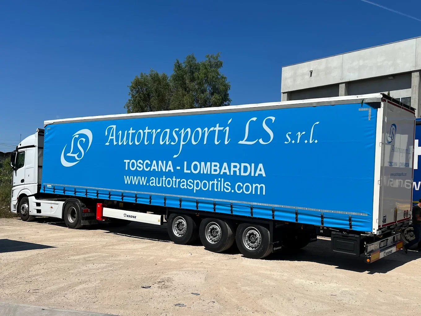 Un camion con scritte blu e bianco della società Autotrasporti LS s.r.l., che effettua trasporti tra Toscana e Lombardia, con sito web www.autotrasportils.com, parcheggiato su una superficie di terra.