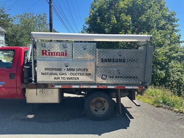 A service truck parked on the street with signs for Rinnai and Samsung HVAC, with details about propane, mini splits, natural gas, ducted air, and water heating.
