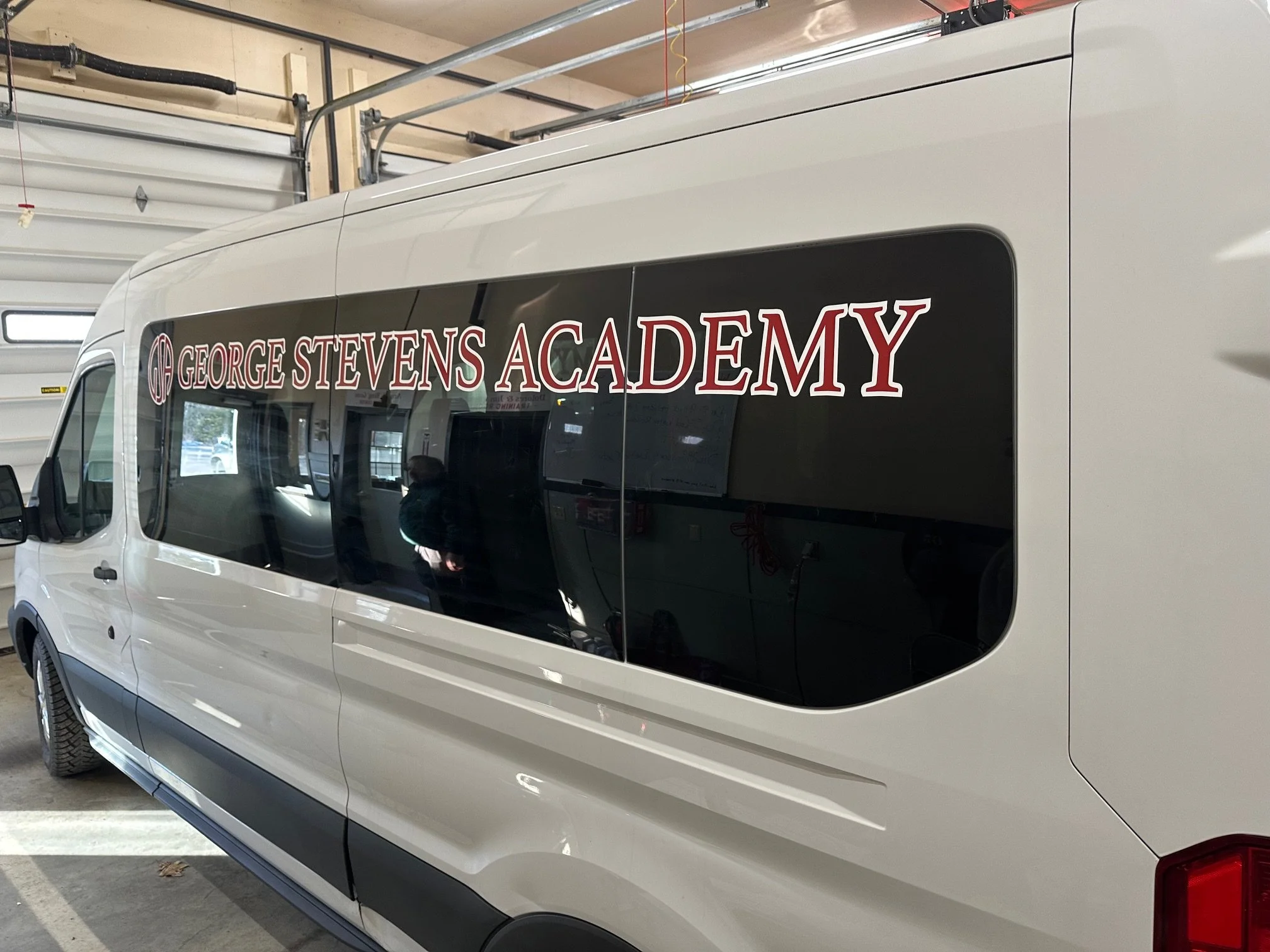 White van inside a garage with windows, displaying 'George Stevens Academy' text on the side window.