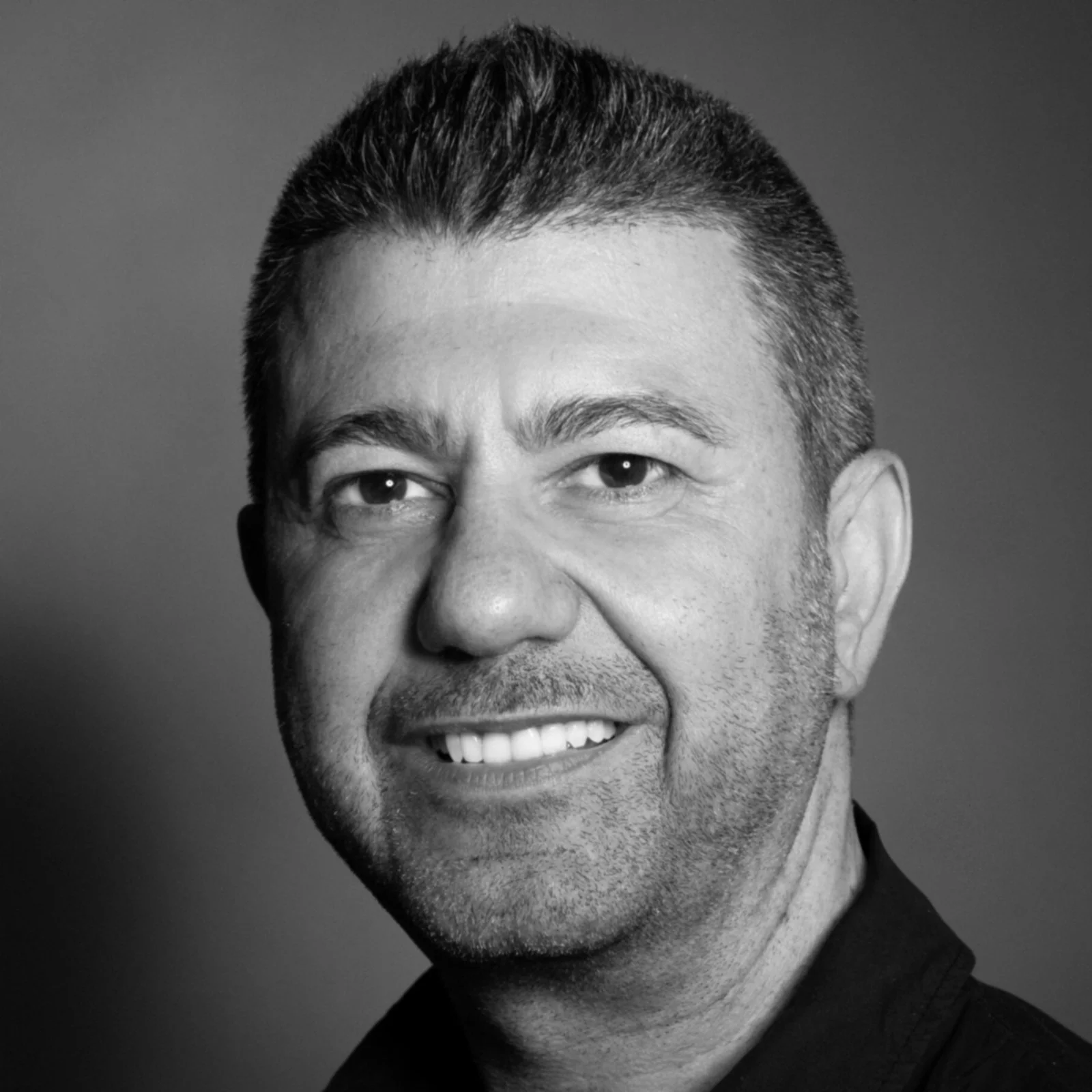 Black and white photo of a smiling man with short hair and facial stubble.