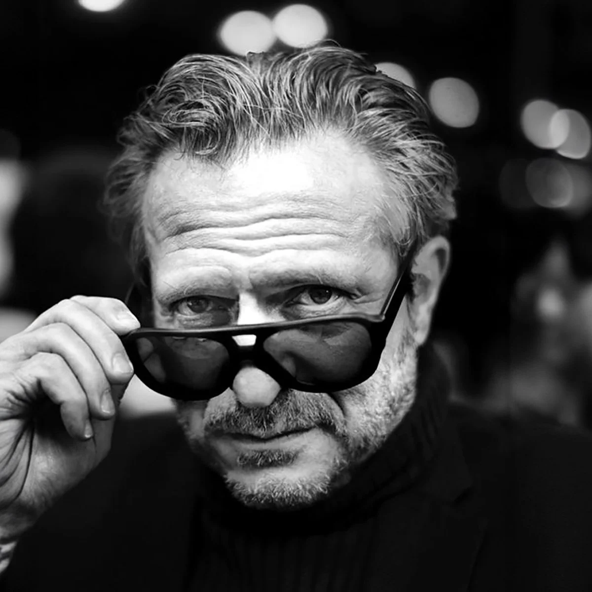 Black and white photo of a man wearing sunglasses, looking over the top, with a serious expression.