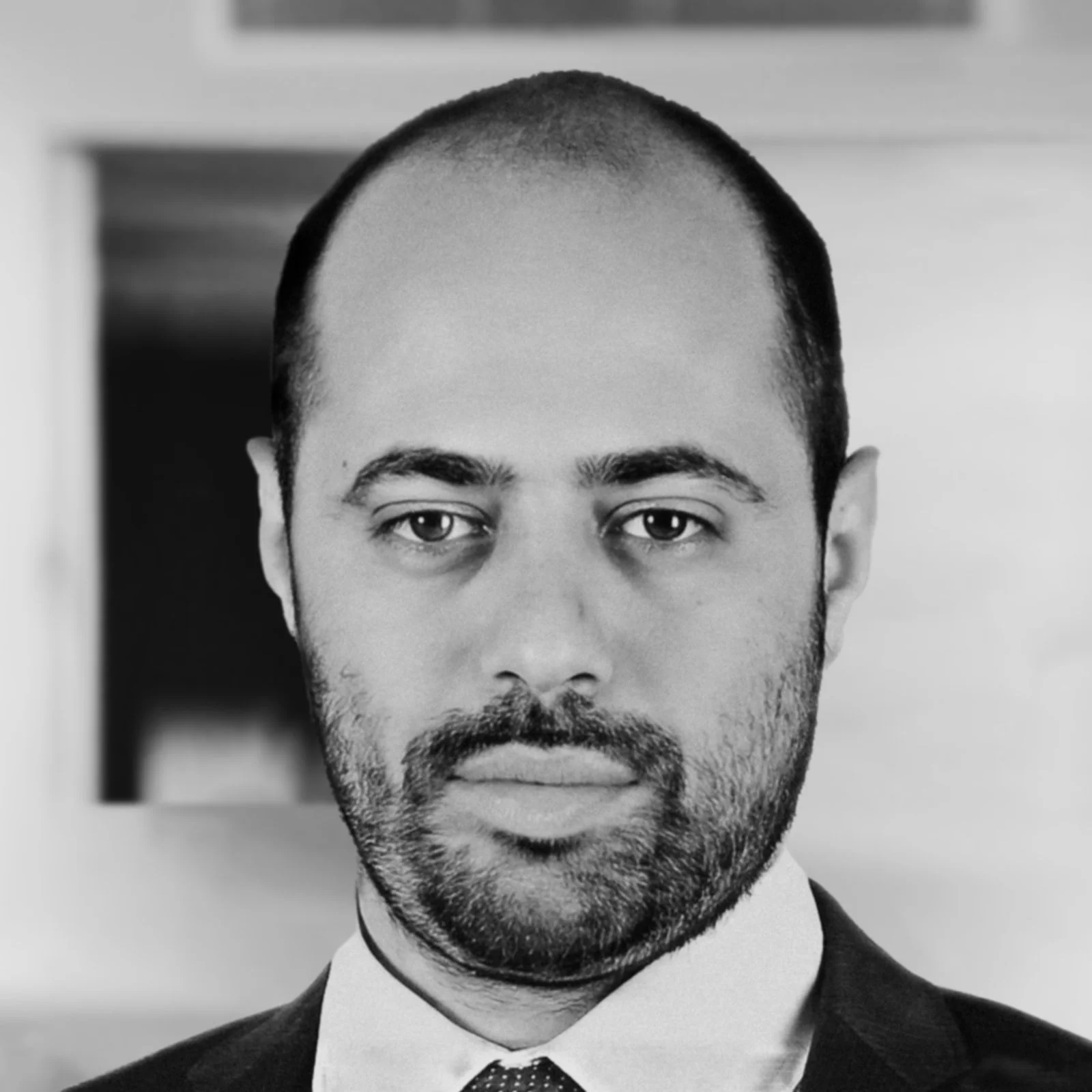 Black and white portrait of a man with a beard, wearing a suit, looking directly at the camera.