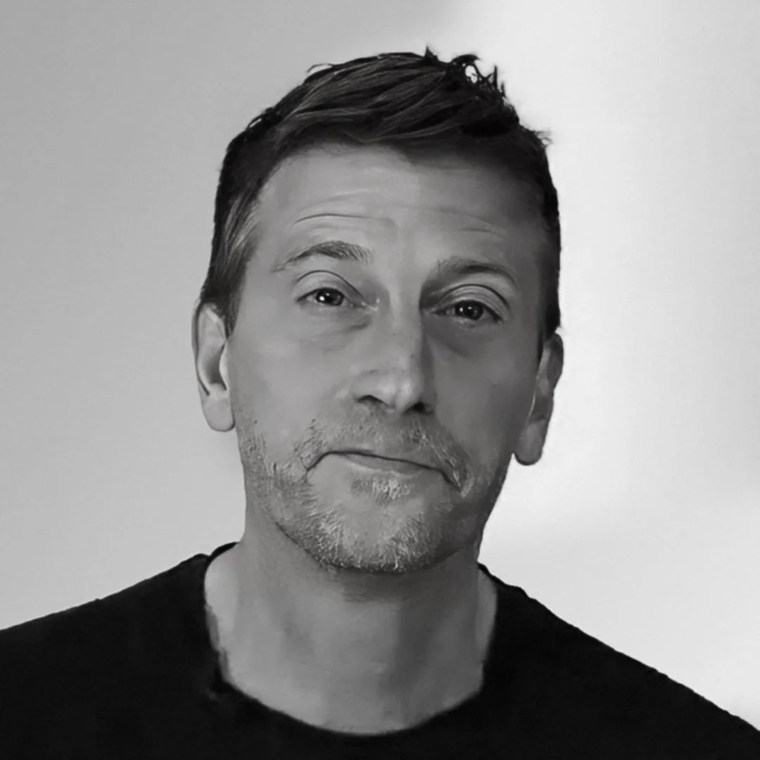 Black and white portrait of a middle-aged man with short hair, wearing a dark shirt, neutral expression, light background.