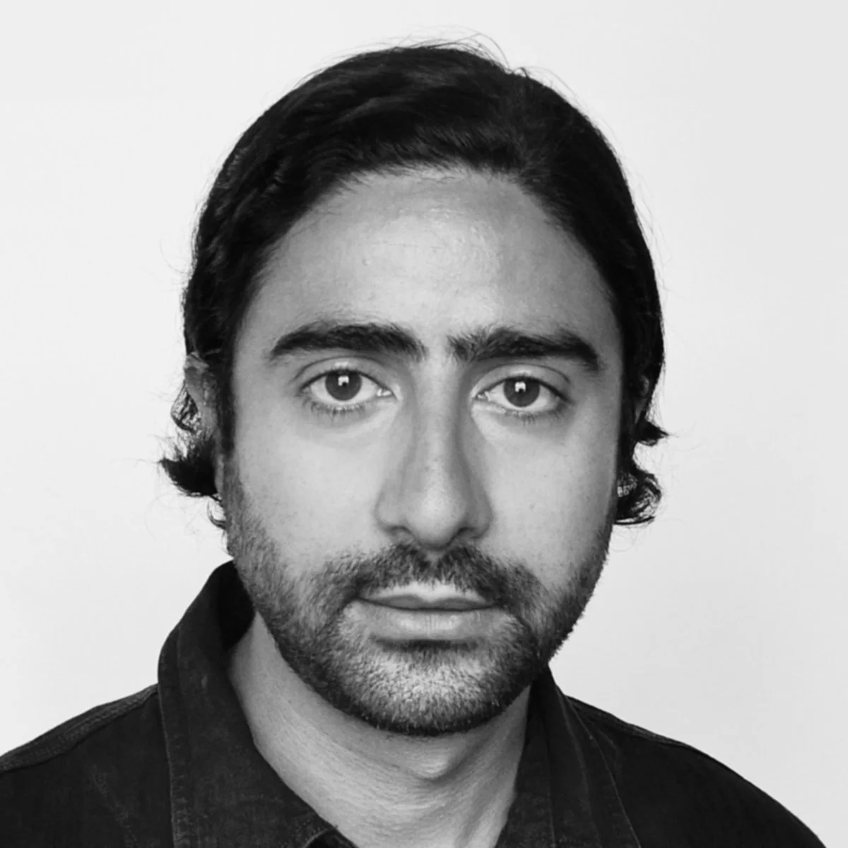 Black and white portrait of a man with medium-length hair and a beard, wearing a dark shirt.