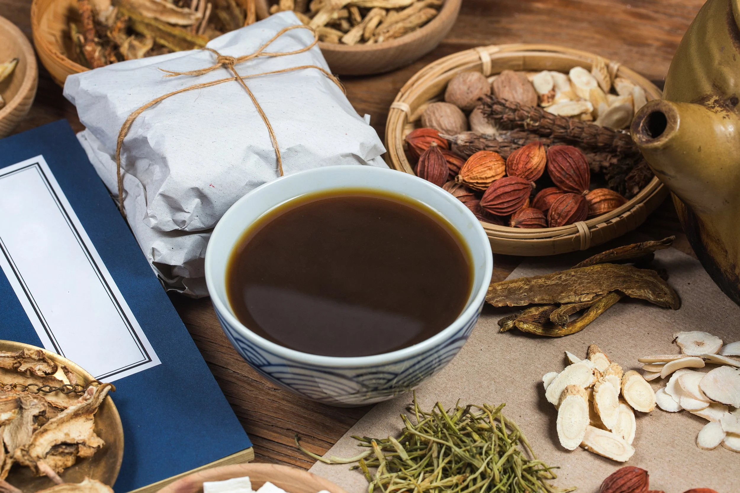 A cup of black coffee surrounded by various herbs, spices, and dried botanicals on a wooden table.
