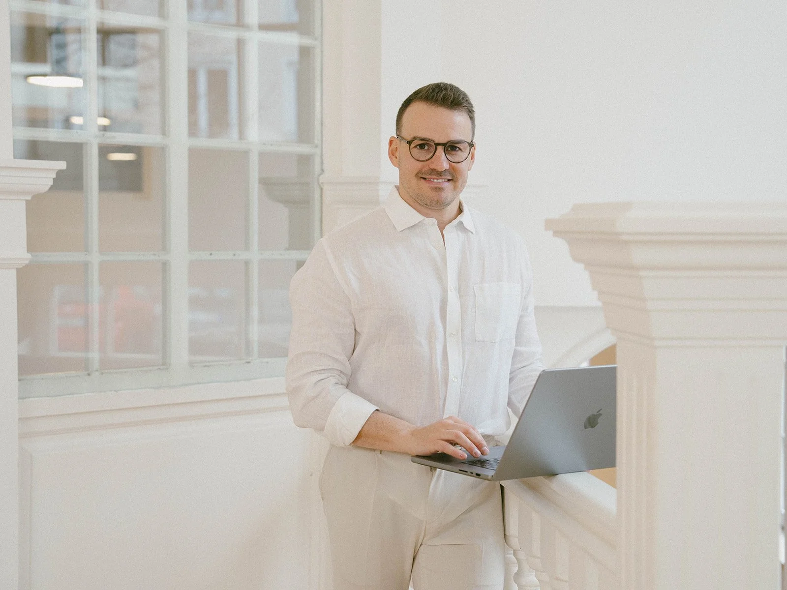 Mann mit Laptop in einem hellen, eleganten Innenraum am Fenster.