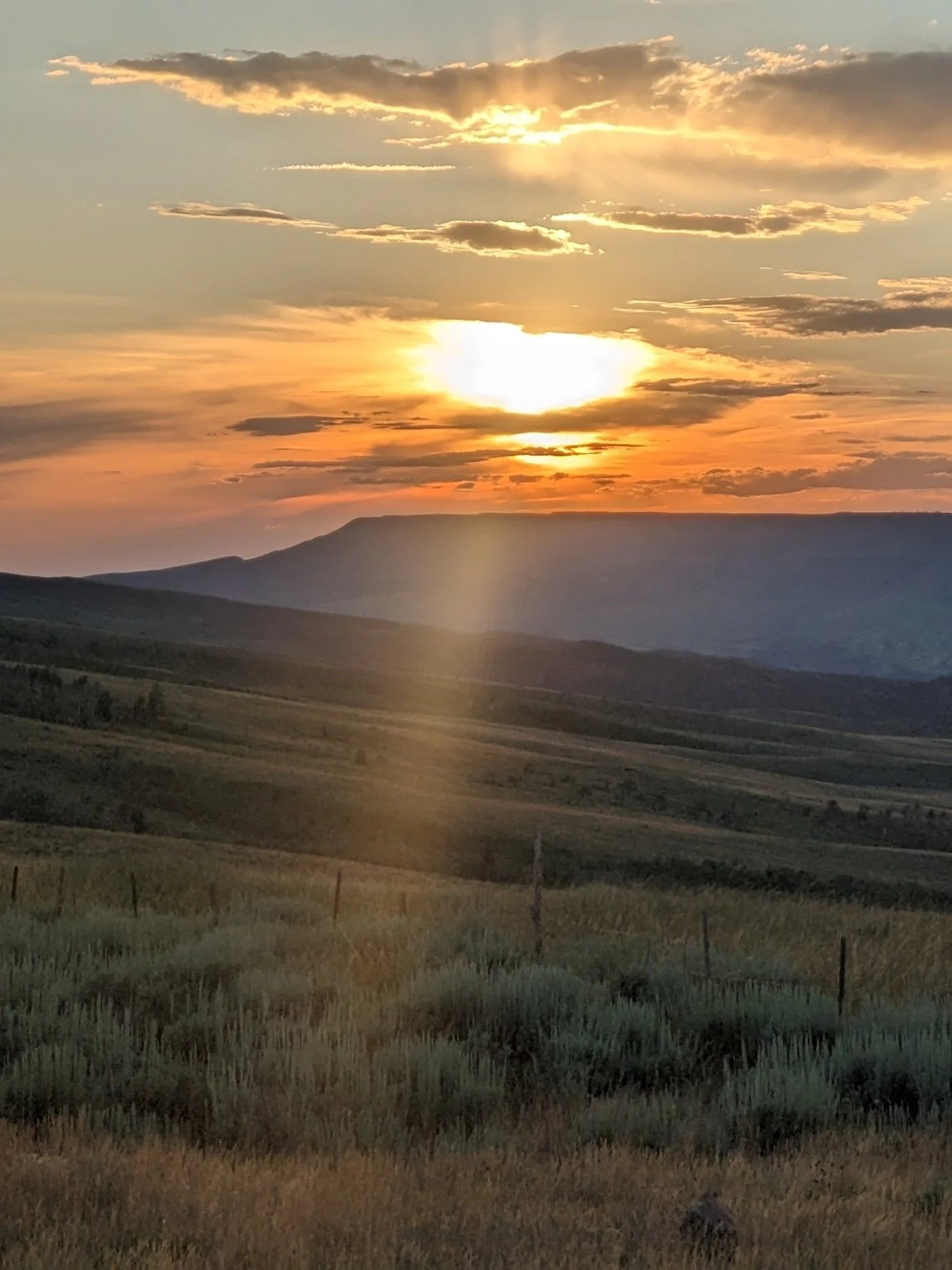 Sunset over rolling hills with scattered clouds in the sky.