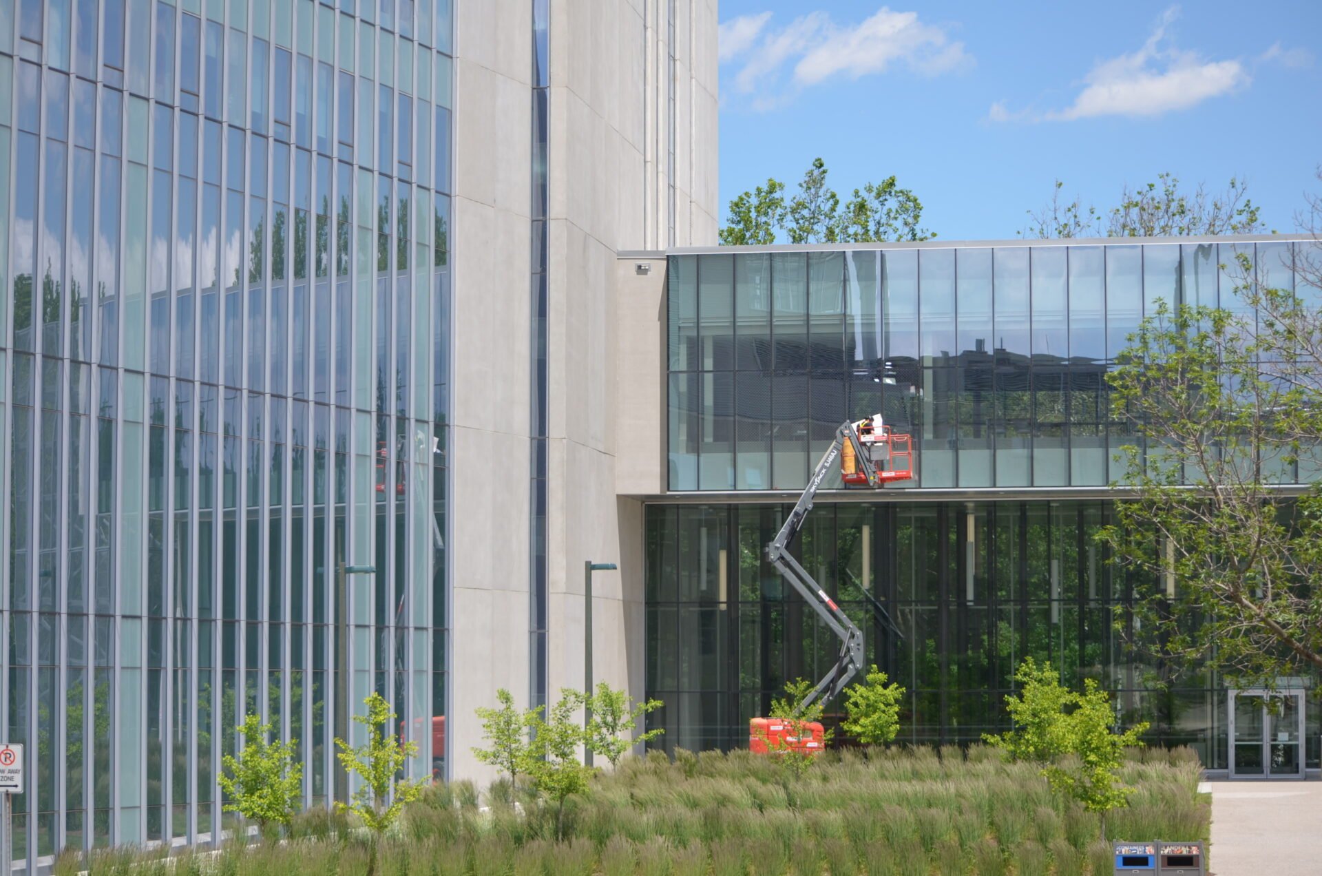 Bird-safe window retrofit happening at Western University, a worker up on a mechanical ladder assessing windows on all glass building
