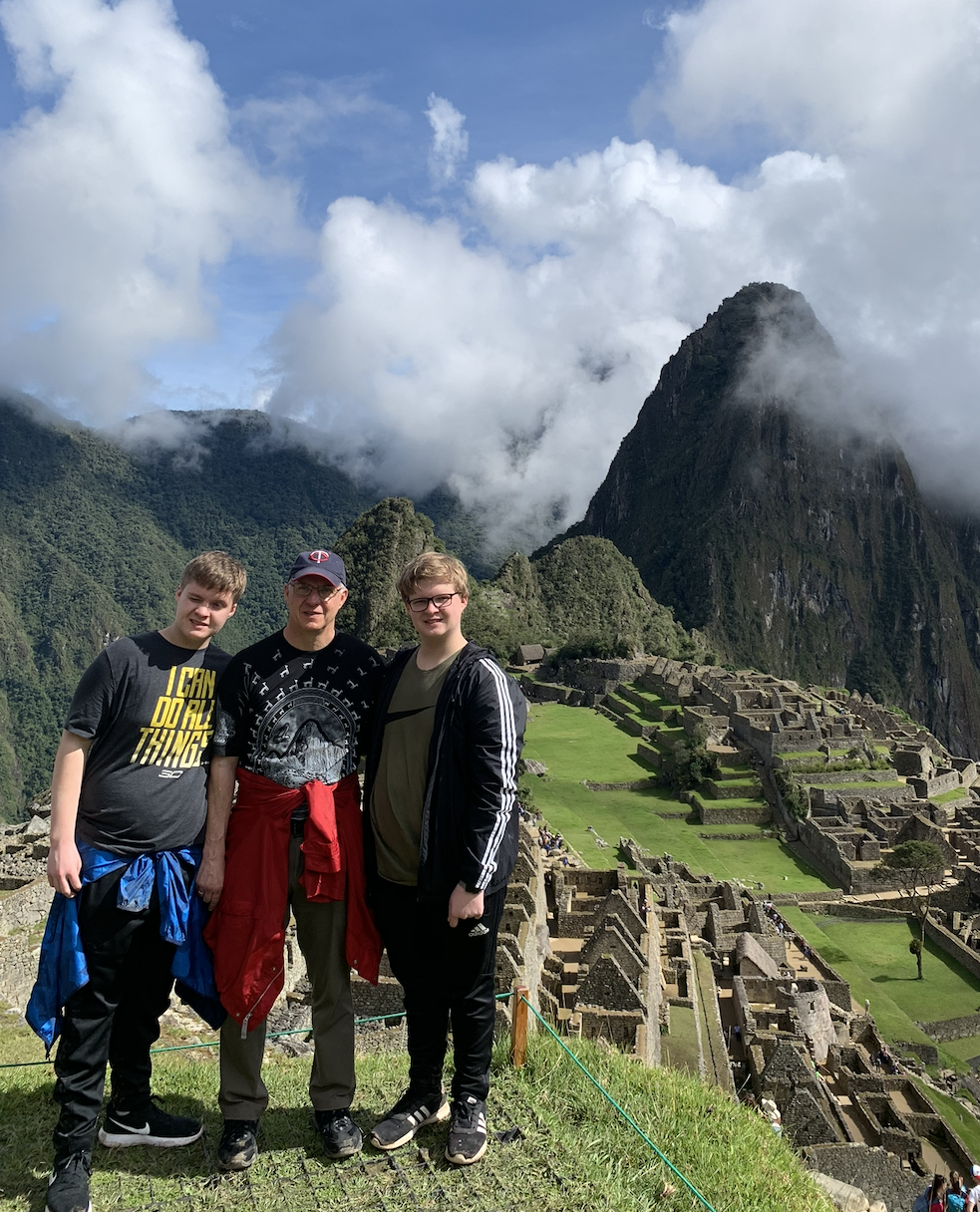 Three people standing in front of Machu Picchu with mountains and clouds in the background.