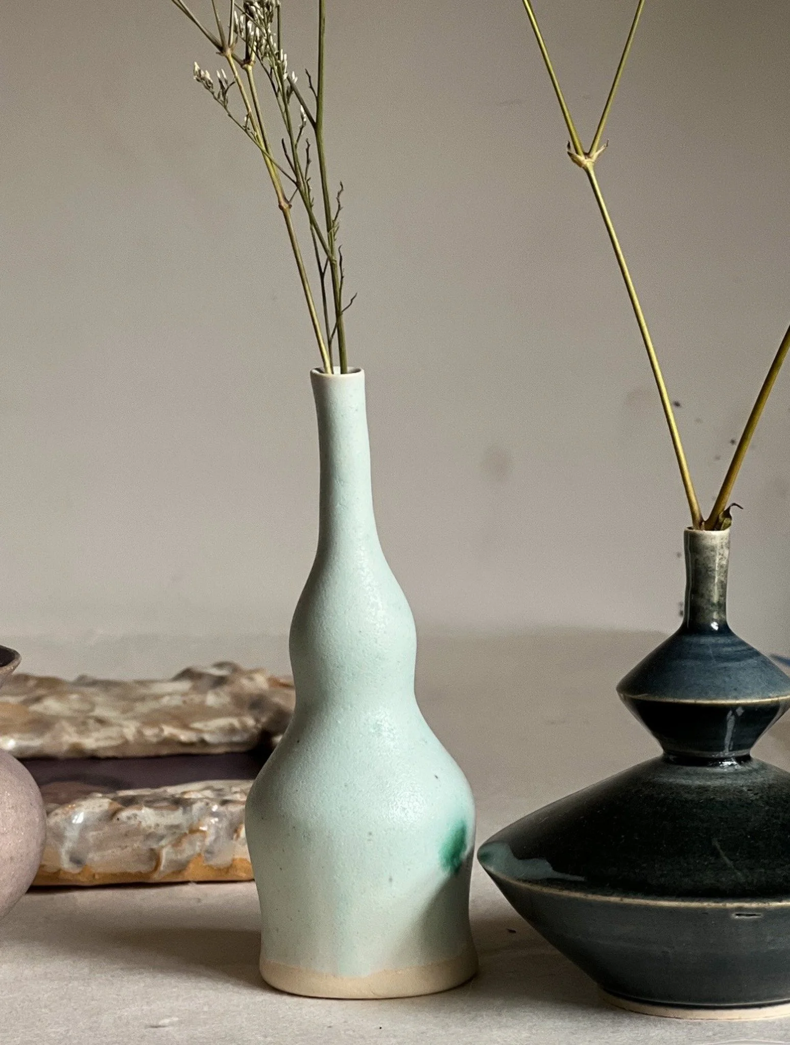 Stylized ceramic vases with dried branches, set on a flat surface.