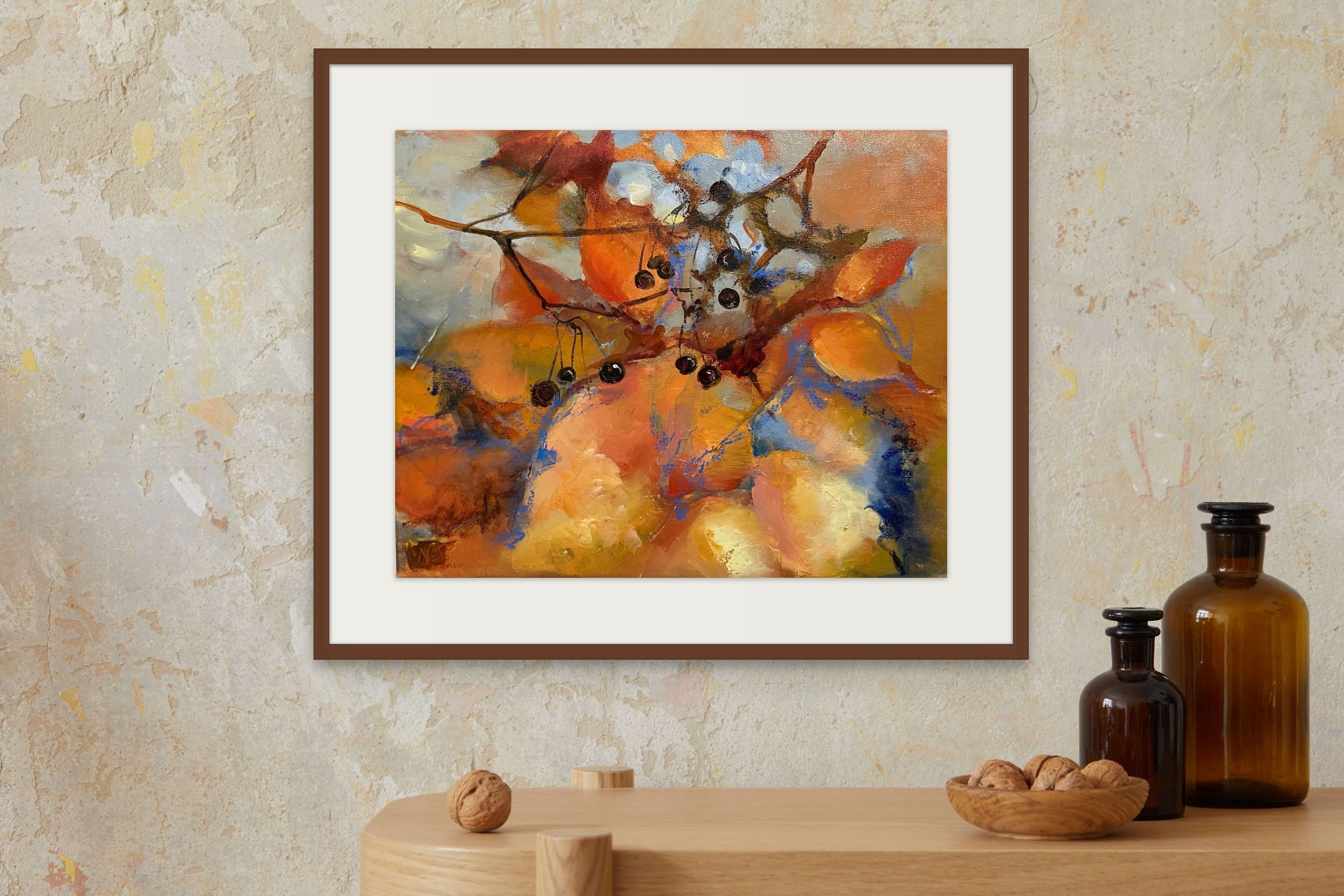Abstract painting of orange and blue leaves and berries hanging from branches displayed on a wall with a beige textured finish, with vases and a bowl of walnuts on a wooden table below.