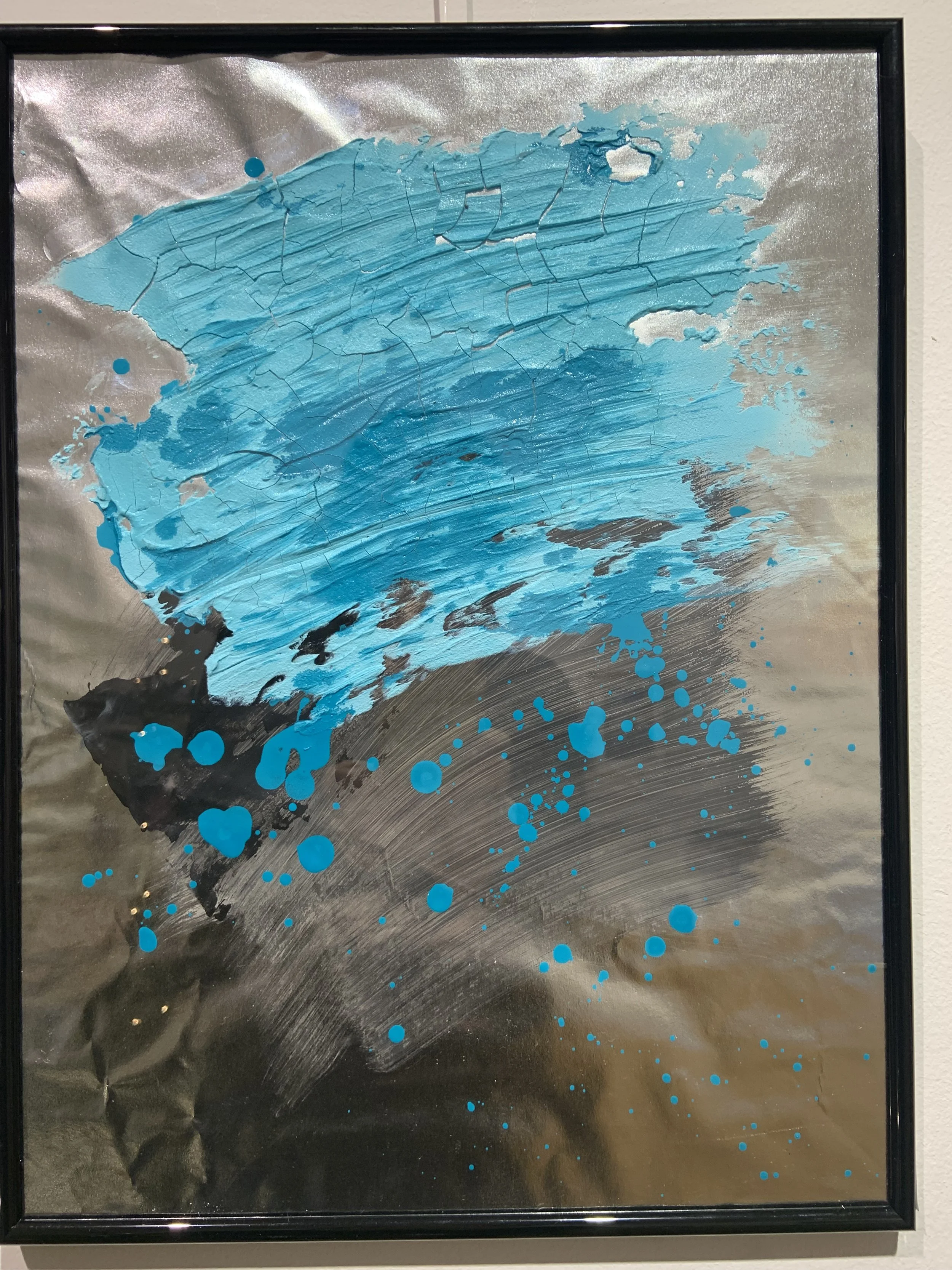 Abstrakt kunstværk med blå, sort og grå maling på metal- eller aluminiumsbaggrund, der viser tekstur og sprøjtede maleffekter.