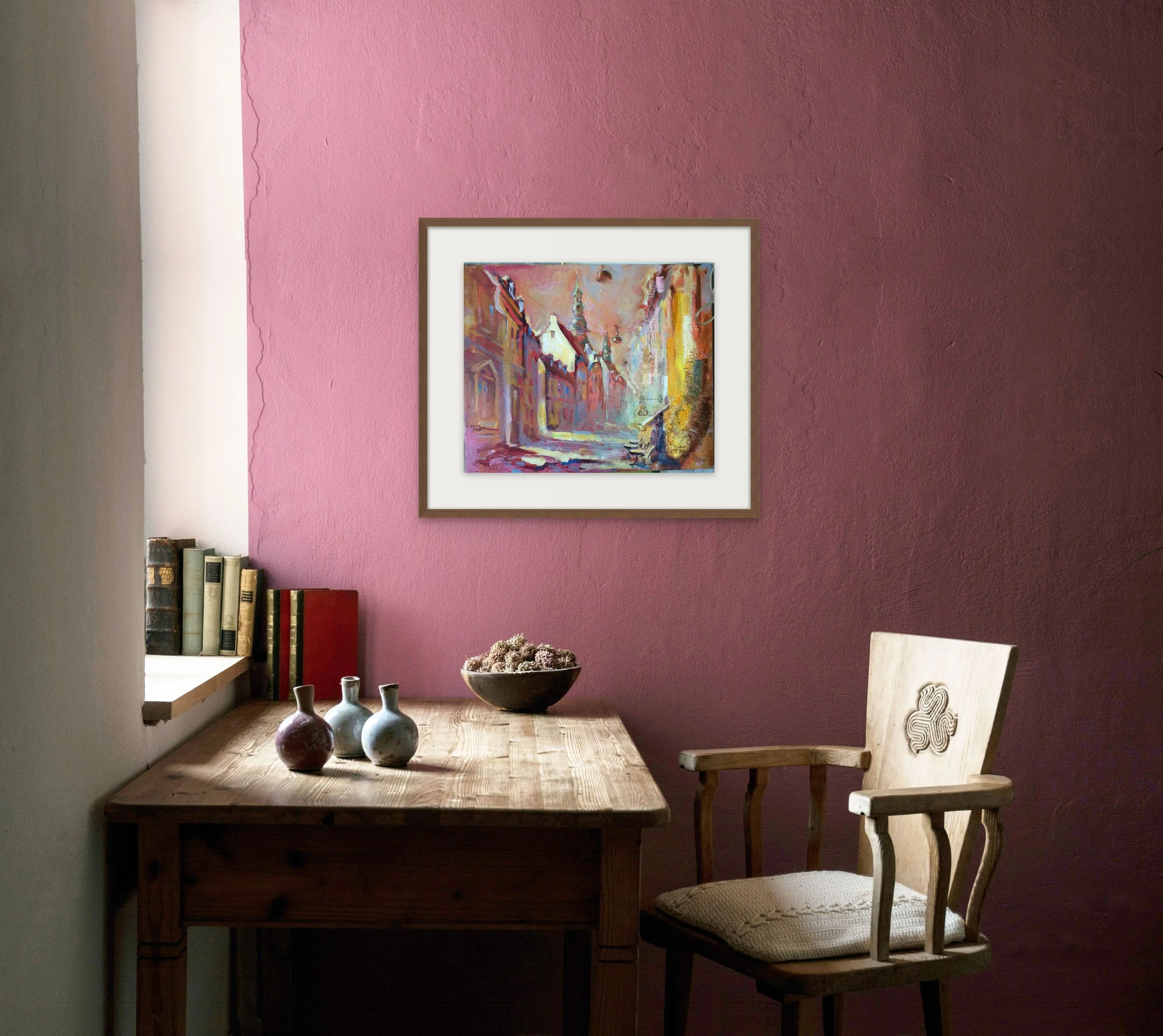 Interior scene with a wooden table topped with vases and a bowl, a wooden chair with cushioned seat, pink wall with artwork, books on window sill.