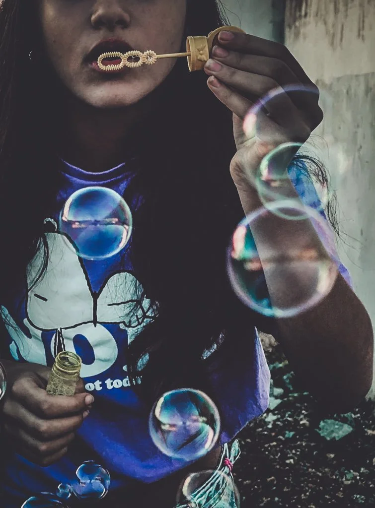 A person is blowing bubbles from a bubble wand, with some bubbles floating in the air around them.