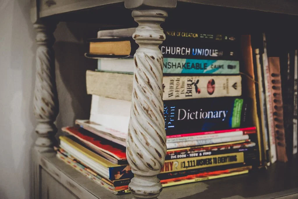 A close-up of a bookshelf with multiple books, with a decorative twisted white wooden support in the foreground.