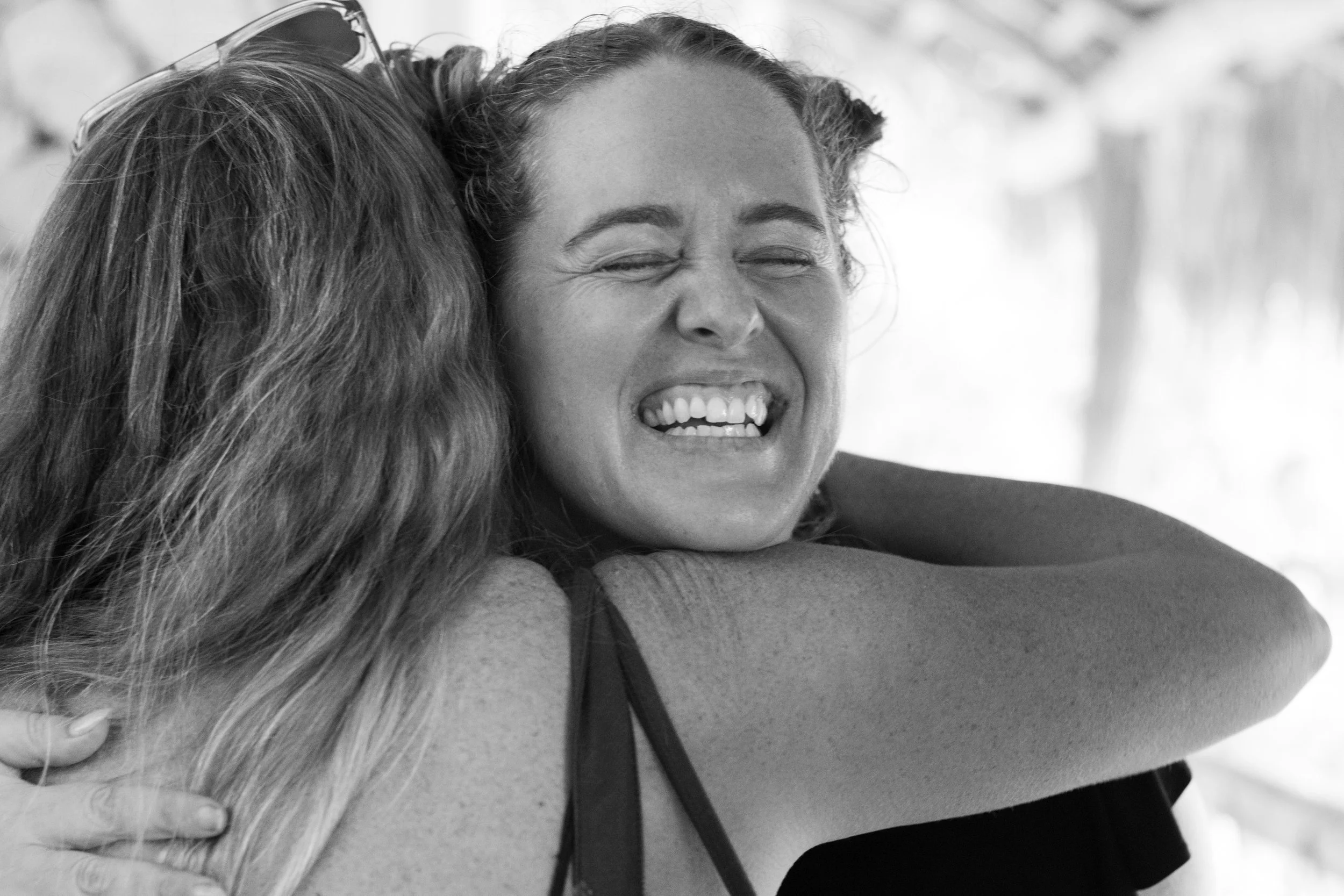Two women hugging, one with her face visible smiling with eyes closed, the other's face not visible, in black and white.