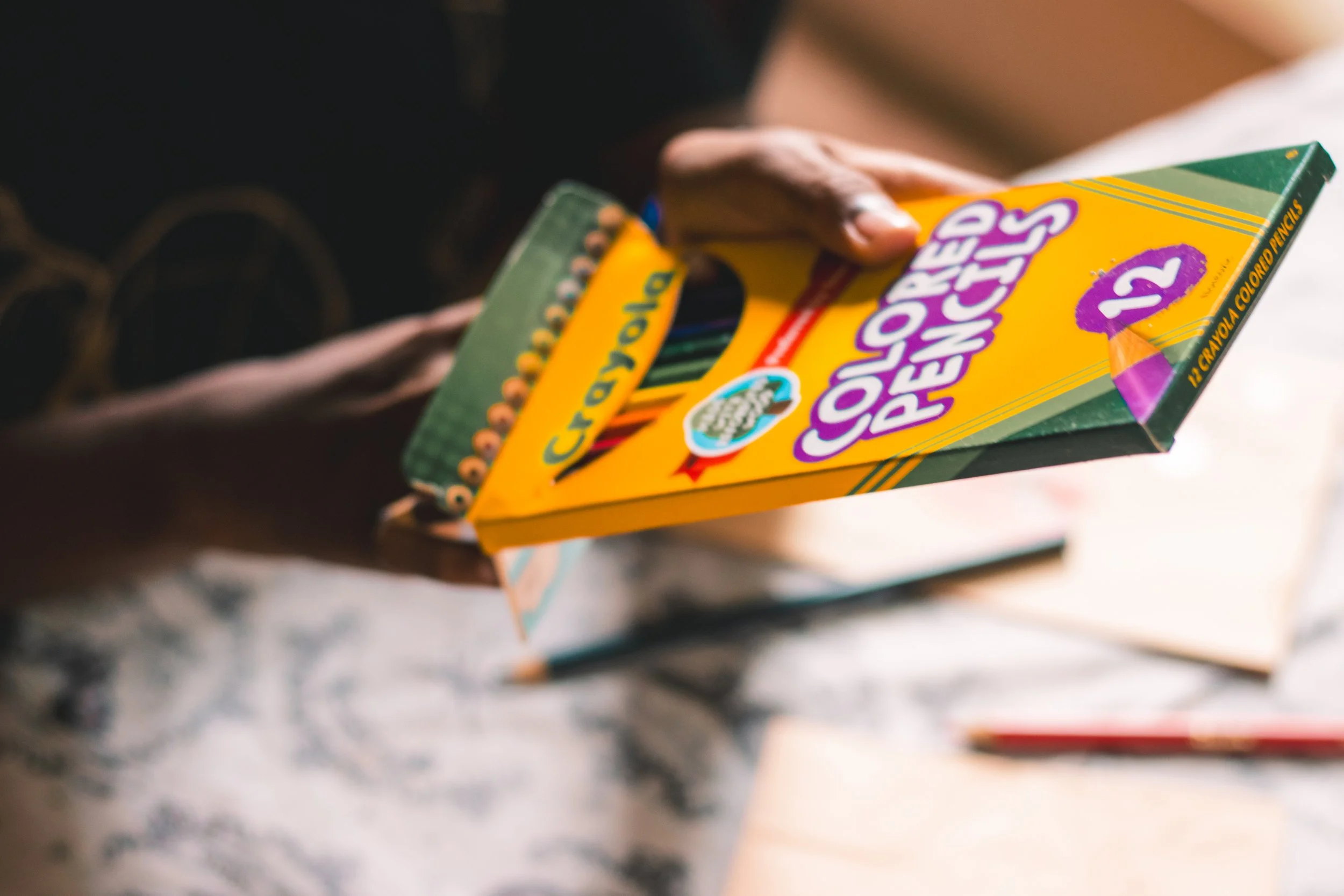 A hand holding a box of Crayola colored pencils marked with the number 12.
