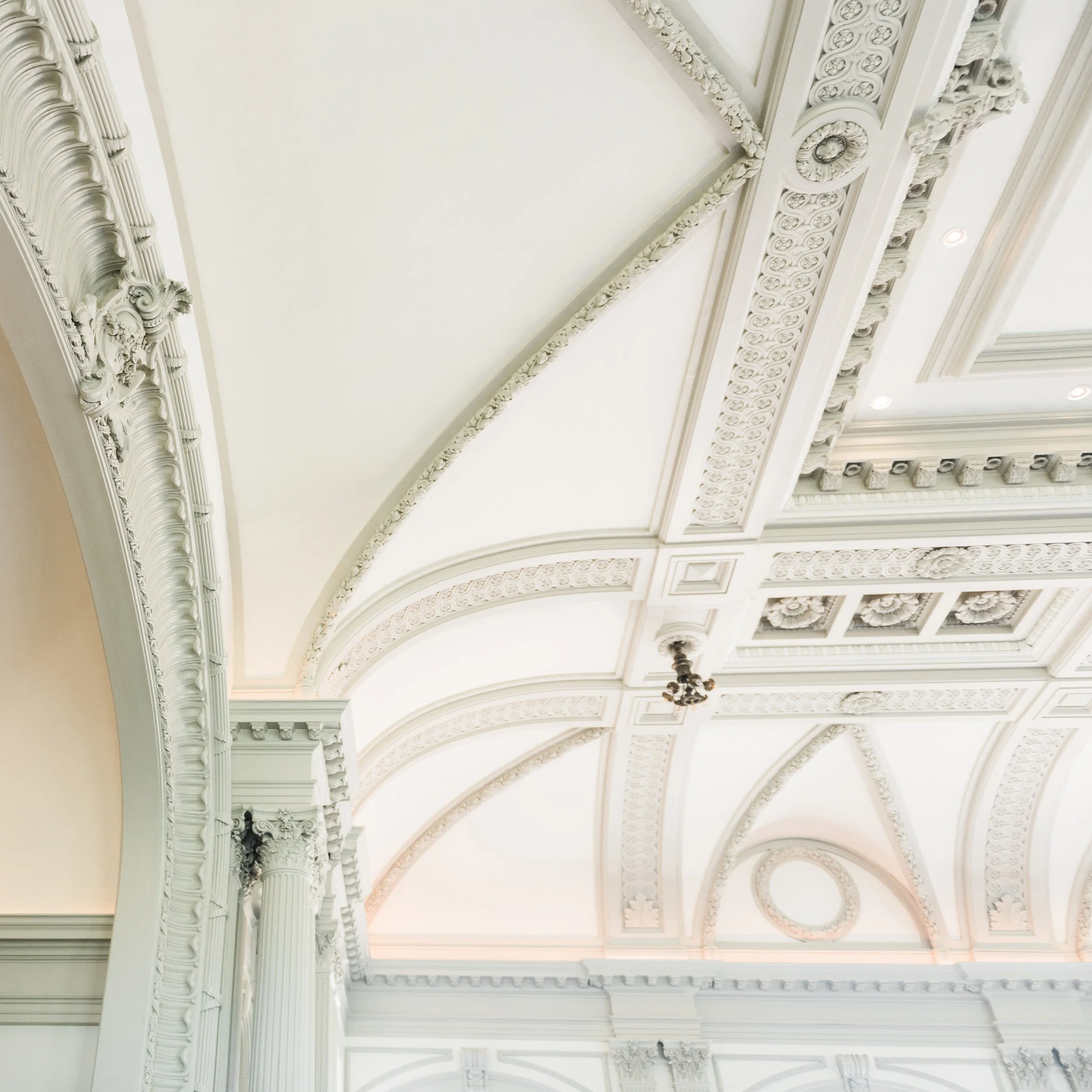 Ornate white ceiling with detailed molding and decorative elements in a grand interior space.