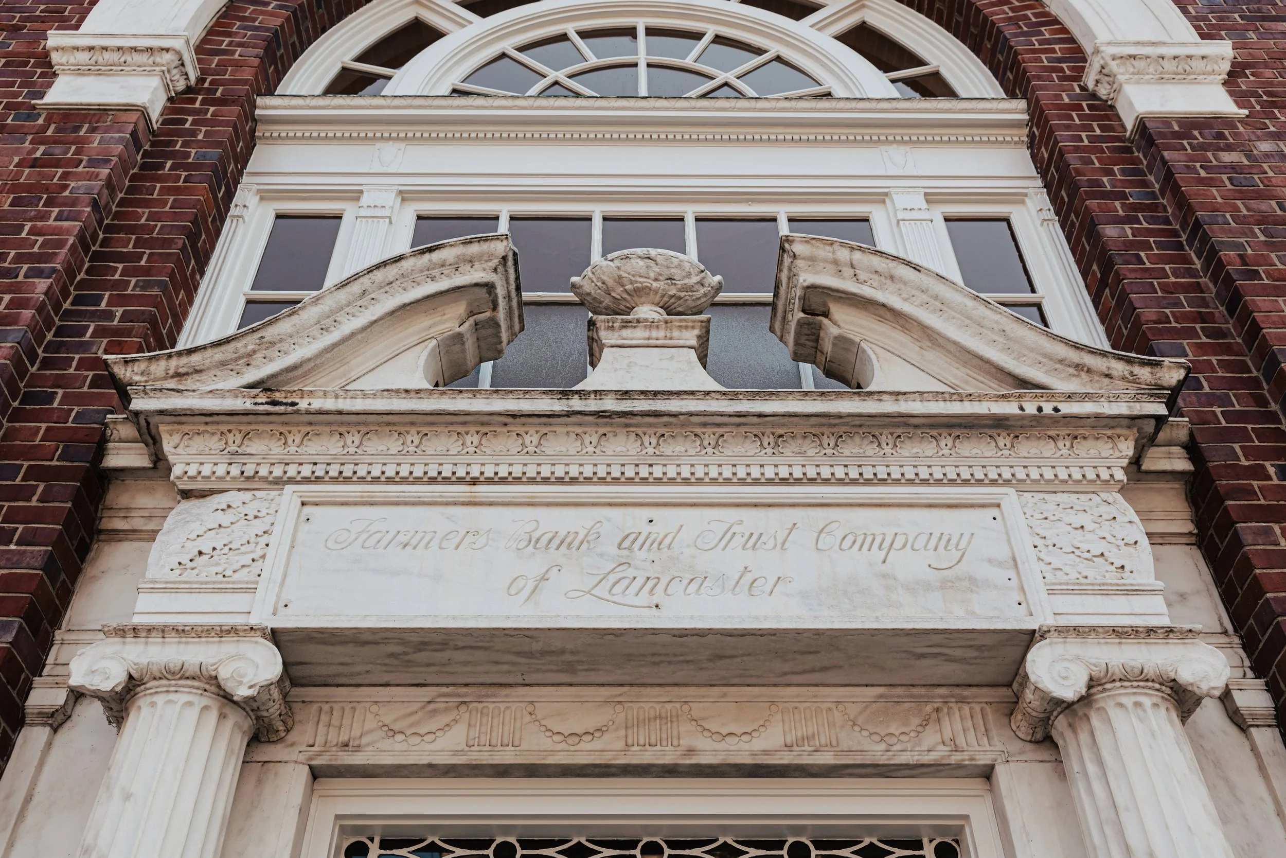 Close-up of the ornate entrance of the Farmers Bank and Trust Company building in Lancaster, featuring classical architecture with columns and decorative carvings, with a sign engraved in the stone.