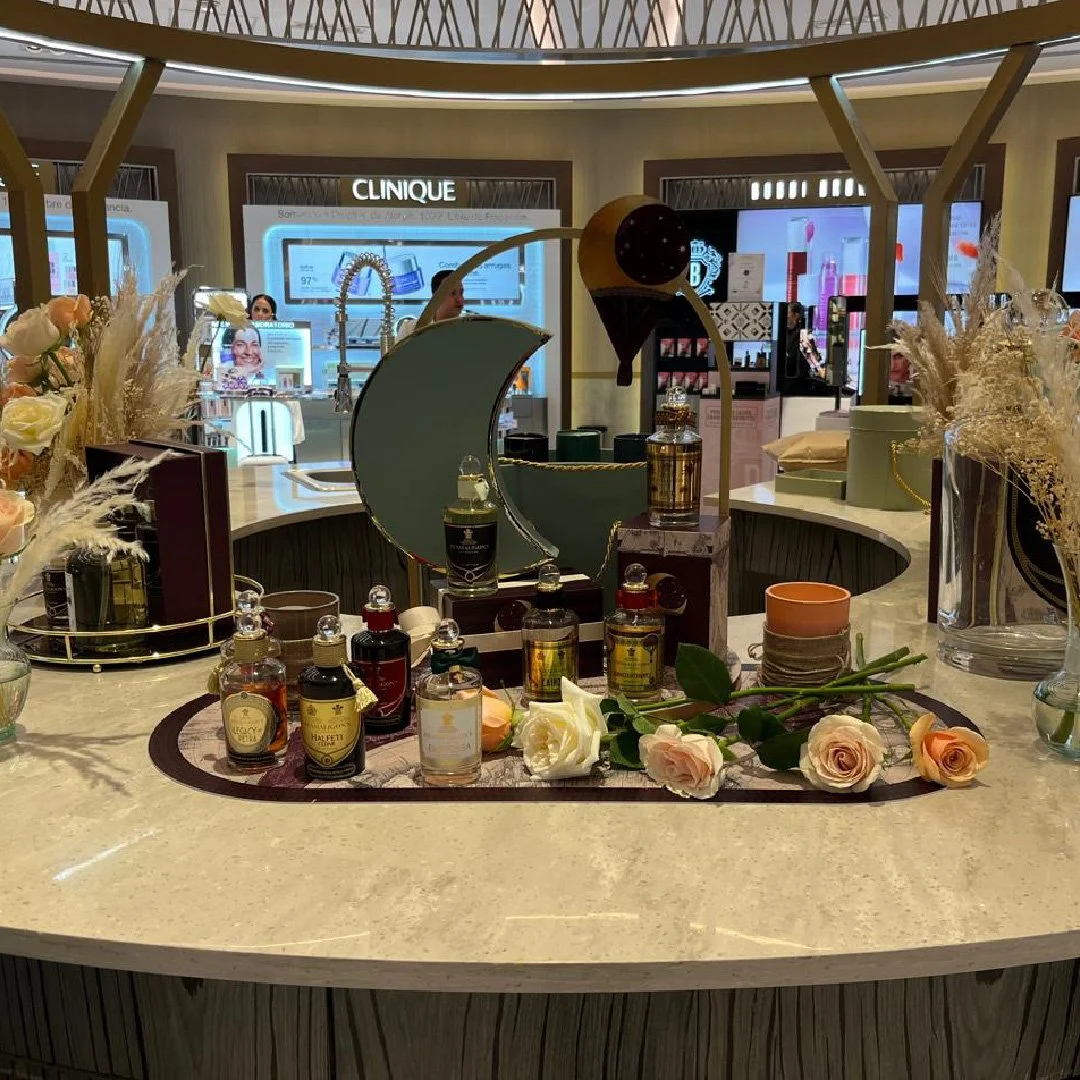 Mostrador de una tienda de perfumes y cosméticos con fragancias, flores y productos en exhibición, en un entorno elegante y bien iluminado.