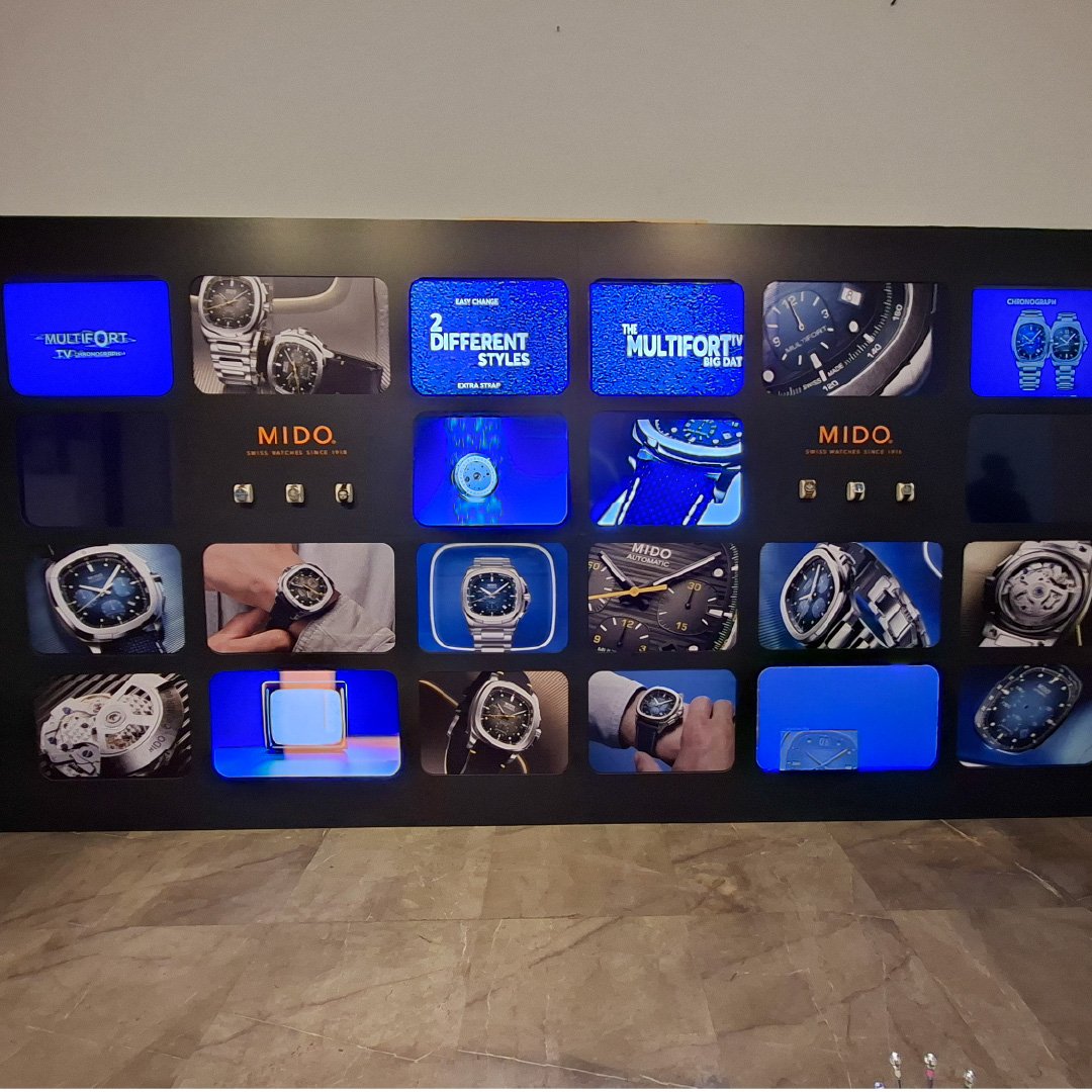 Pared con pantallas que muestran relojes de marca Mido y otras características de relojería, en exhibición