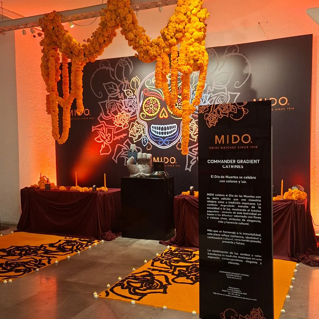 Decoración de Día de Muertos con un mural de calavera colorida, ofrendas con velas y flores de cempasúchil, y un cartel informativo de MIDO en un ambiente con iluminación cálida. para lanzamiento de reloj MIDO