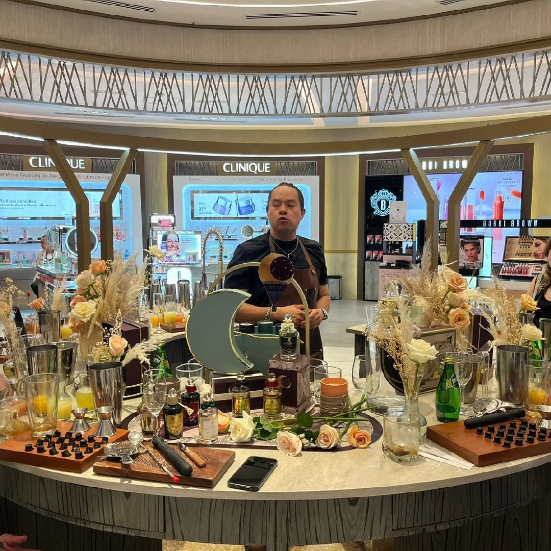 Mostrador de belleza decorado con flores, frascos y utensilios, en un centro comercial. Persona en el fondo en un puesto de productos de belleza de Clinique.