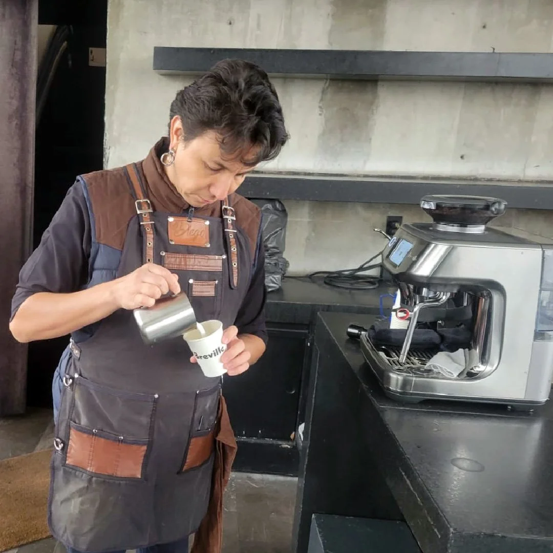 Una mujer sirviendo leche en un vaso con una máquina de café o leche en un establecimiento.