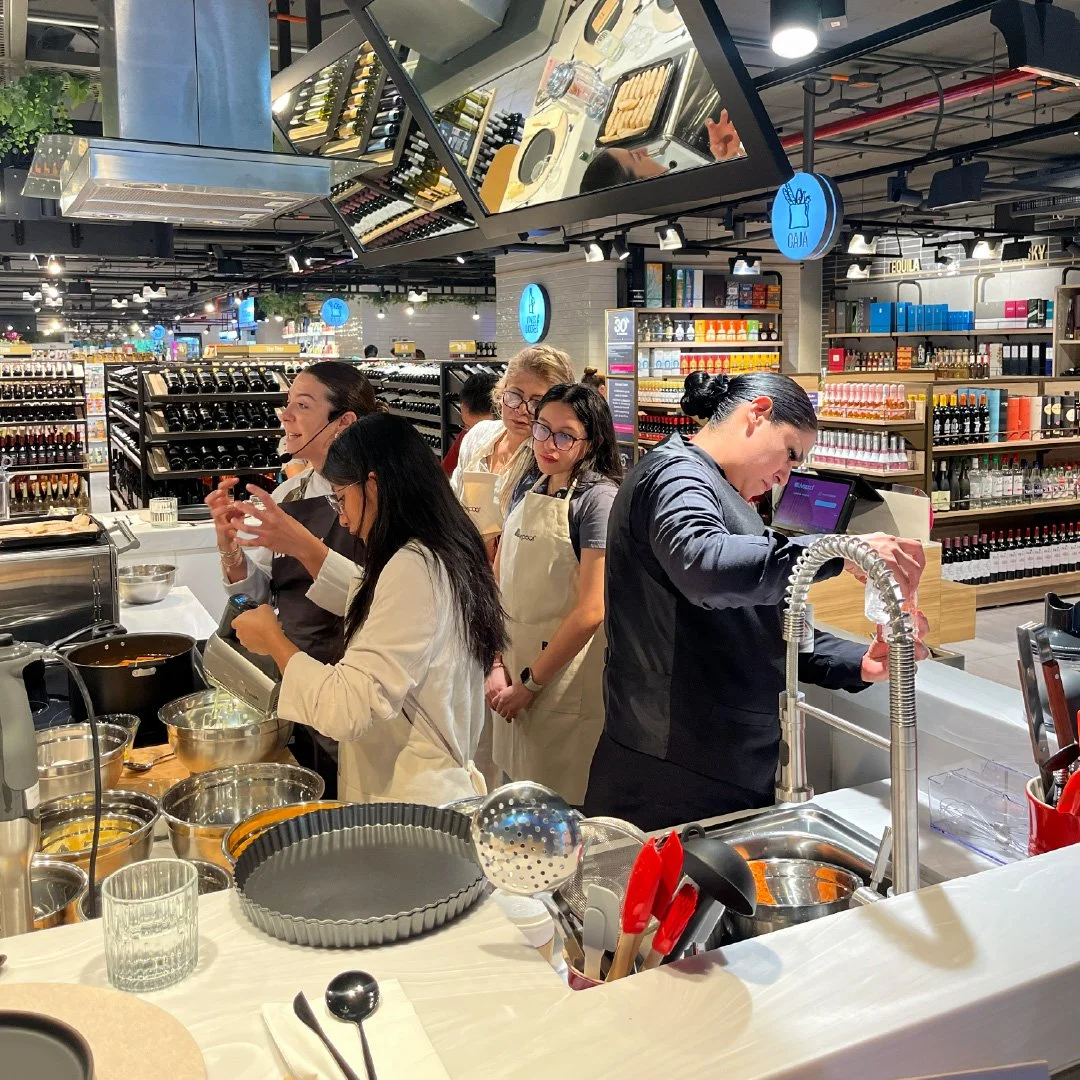 Grupo de personas cocinando y aprendiendo en una estación de cocina en una tienda de supermercado.