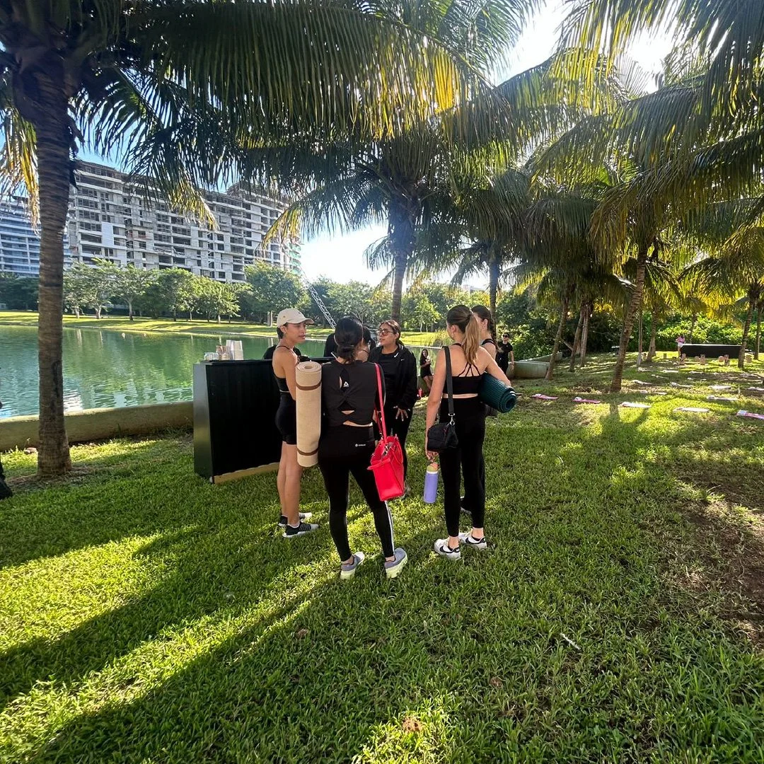 Un grupo de personas prendiendo para una clase de yoga en un parque con árboles palmeras, cerca de un lago, durante el día.