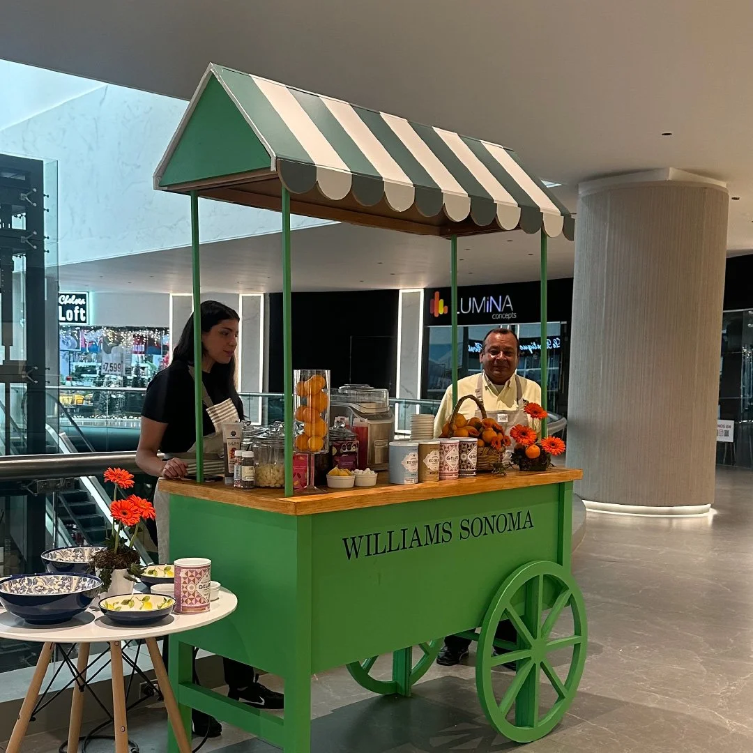 Carrito de venta de frutas y jugos decorado con flores y colores verdes en un centro comercial.