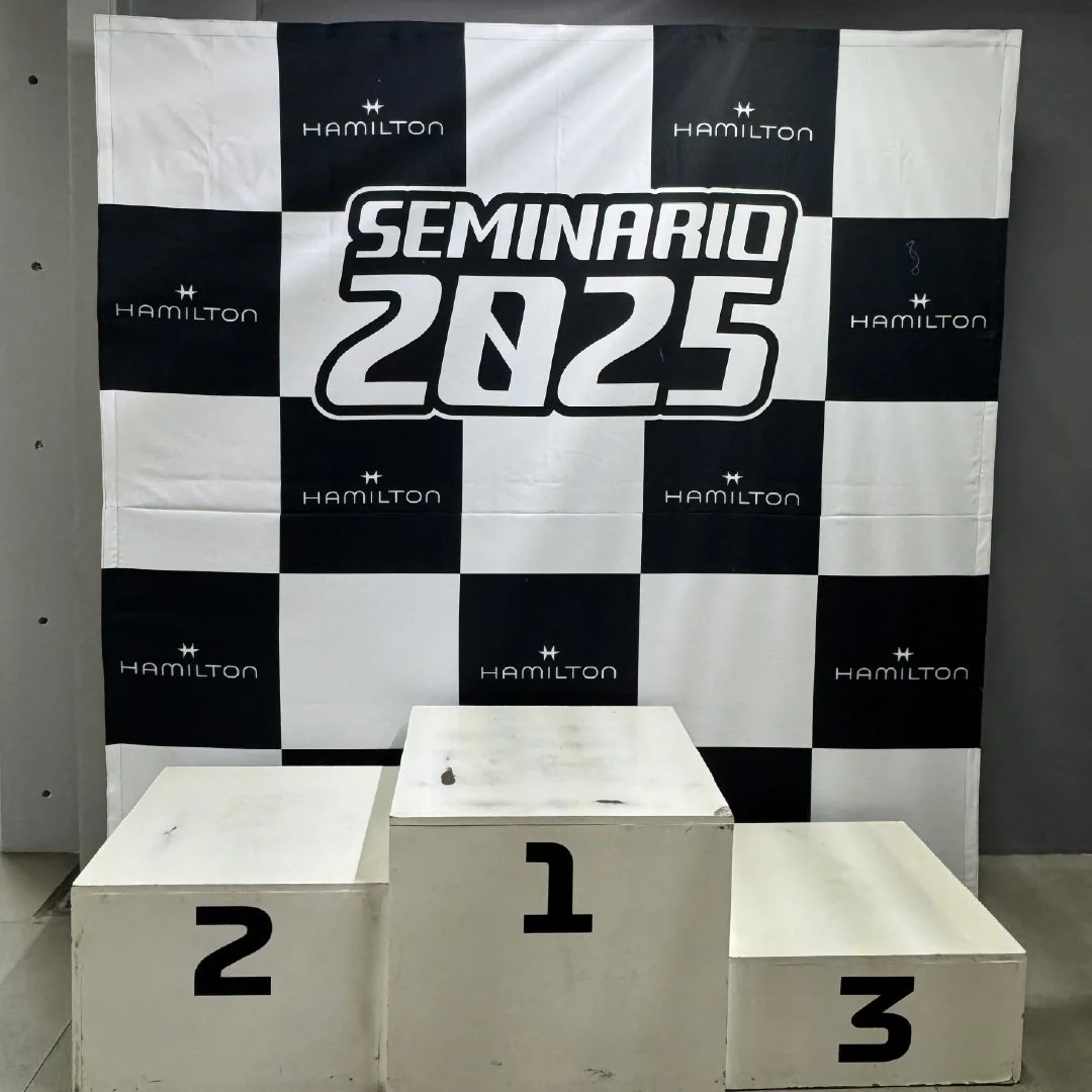 Podios de ganadores con los números 1, 2 y 3 en primer, segundo y tercer lugar, en frente de un fondo con el logo y nombre Hamilton y un cartel que dice 'Seminario 2025'